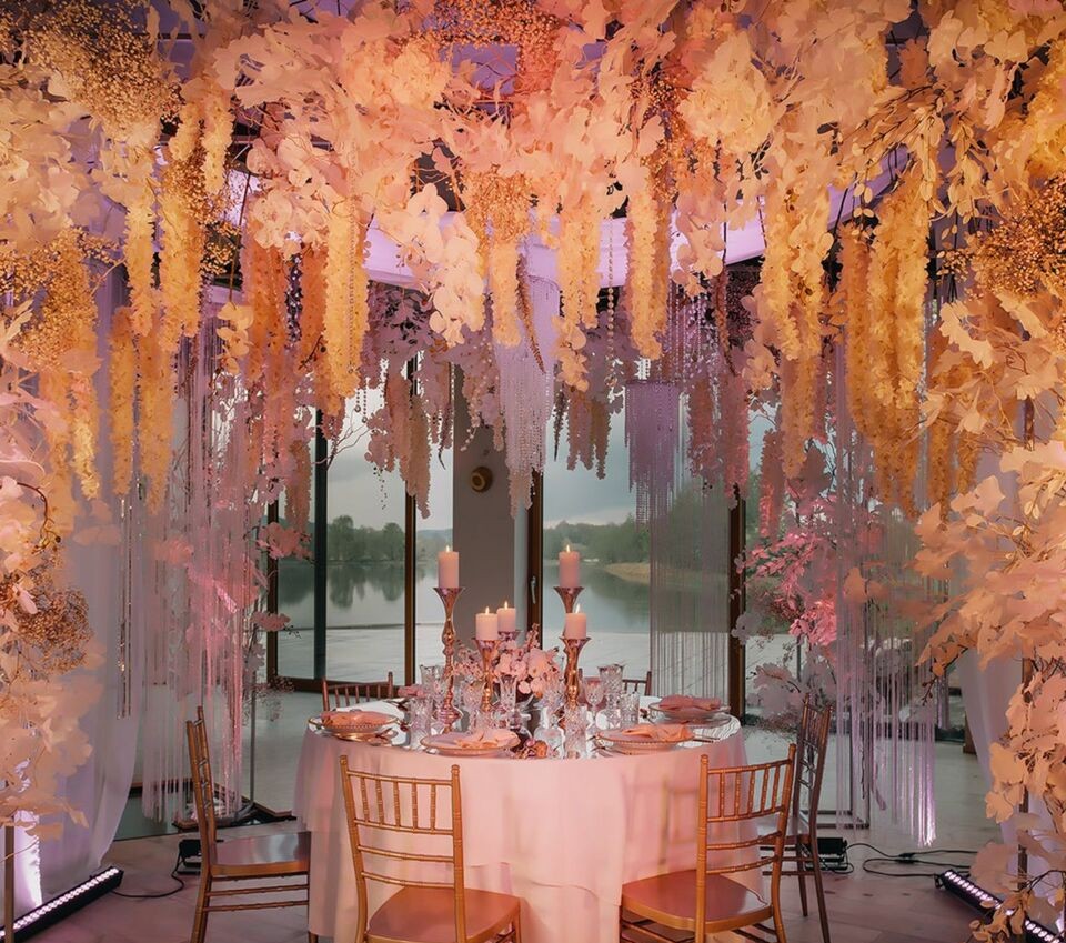 A pyramid stack of empty crystal champagne coupe glasses on a glass table with a dark background and soft lighting.