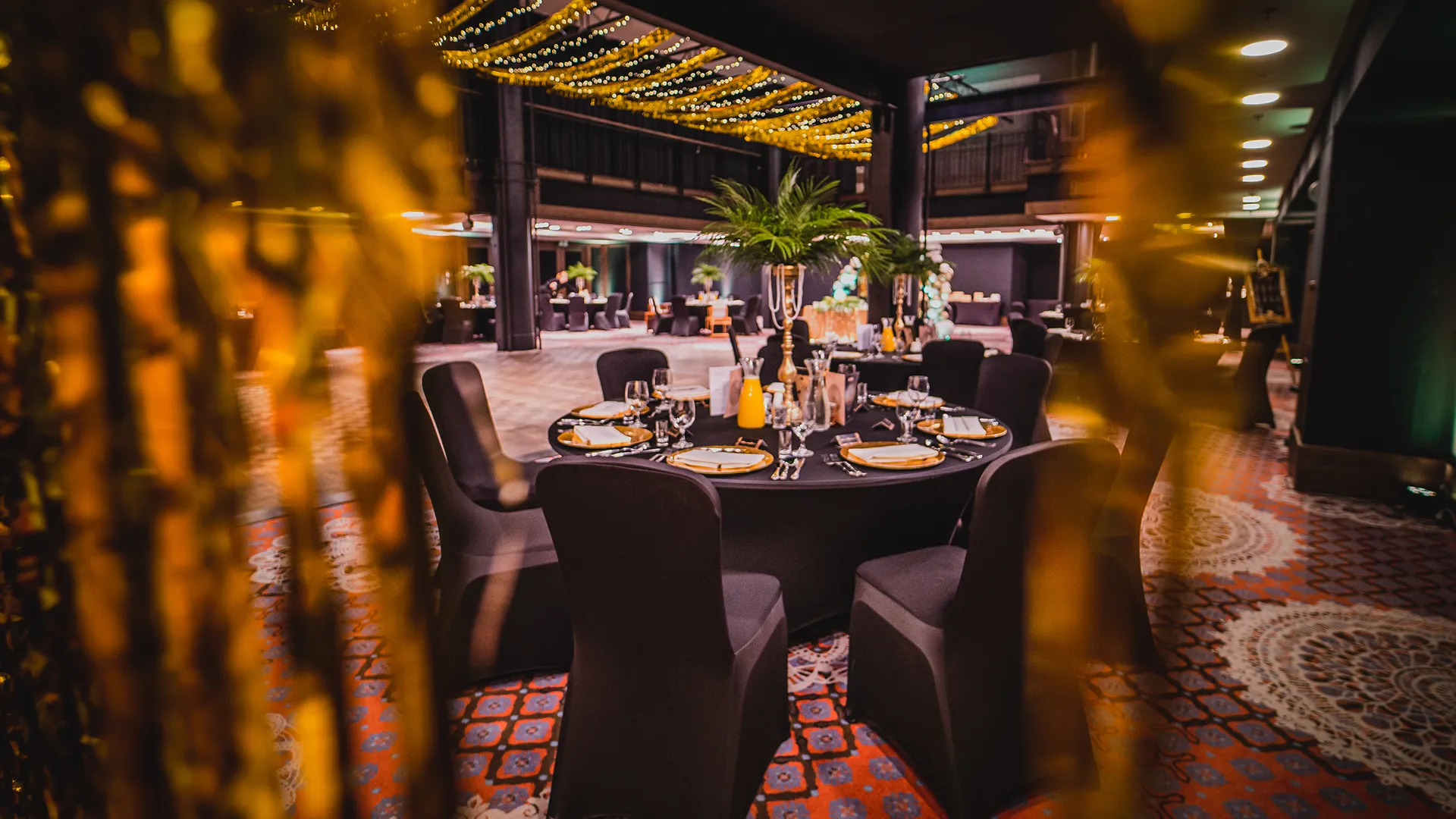 A pyramid stack of empty crystal champagne coupe glasses on a glass table with a dark background and soft lighting.