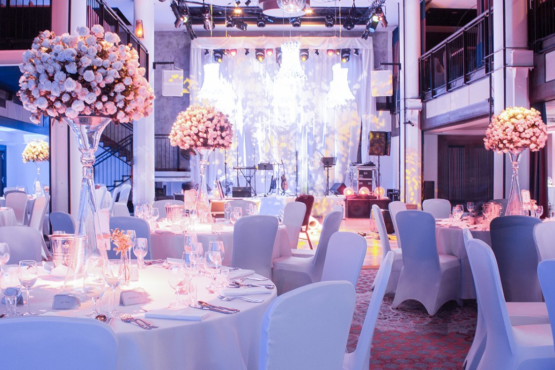 A pyramid stack of empty crystal champagne coupe glasses on a glass table with a dark background and soft lighting.