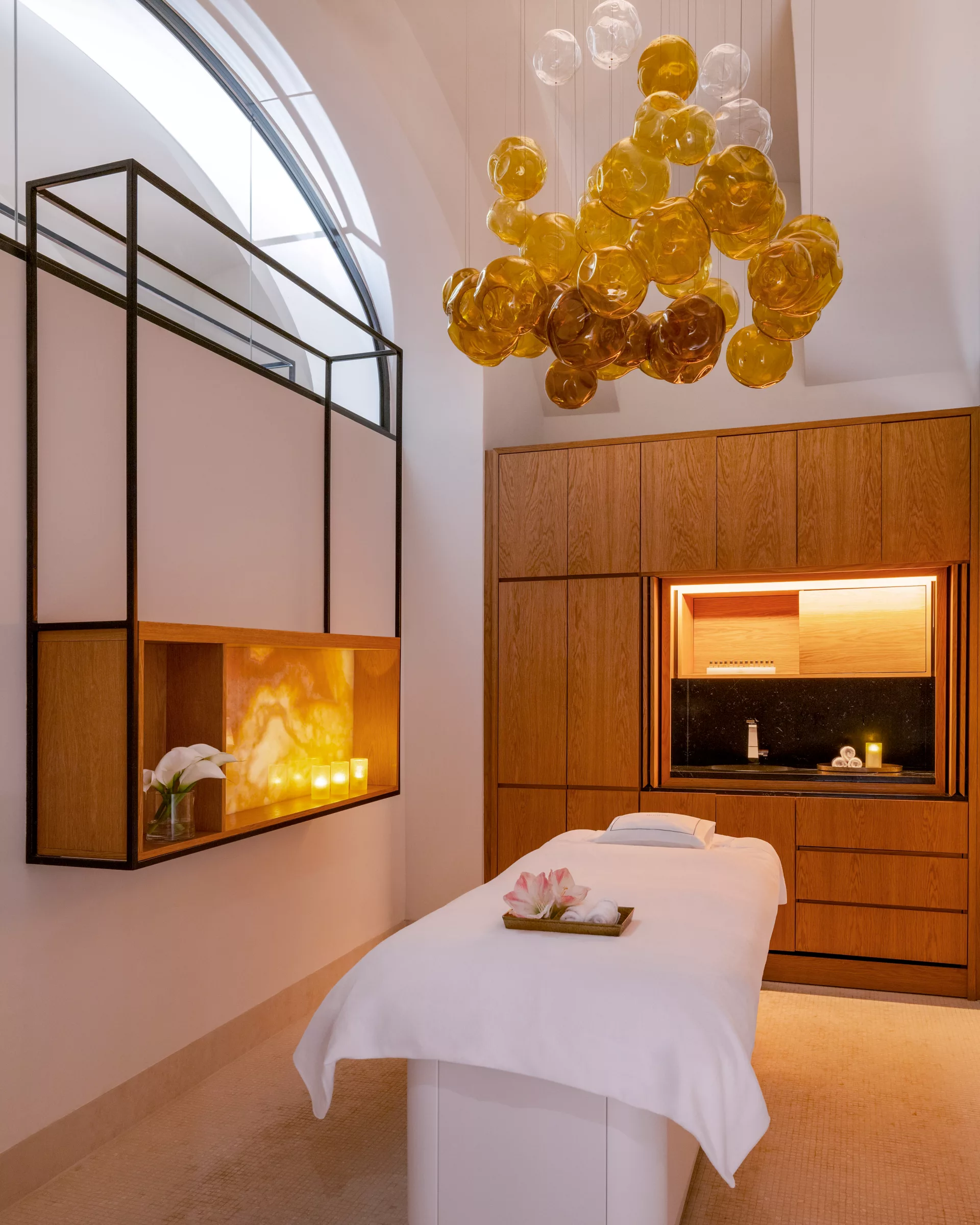 A pyramid stack of empty crystal champagne coupe glasses on a glass table with a dark background and soft lighting.