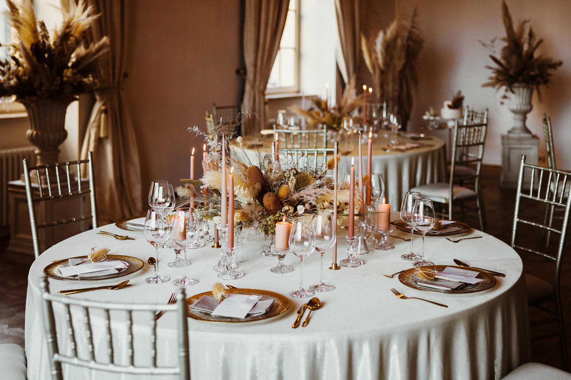 A pyramid stack of empty crystal champagne coupe glasses on a glass table with a dark background and soft lighting.
