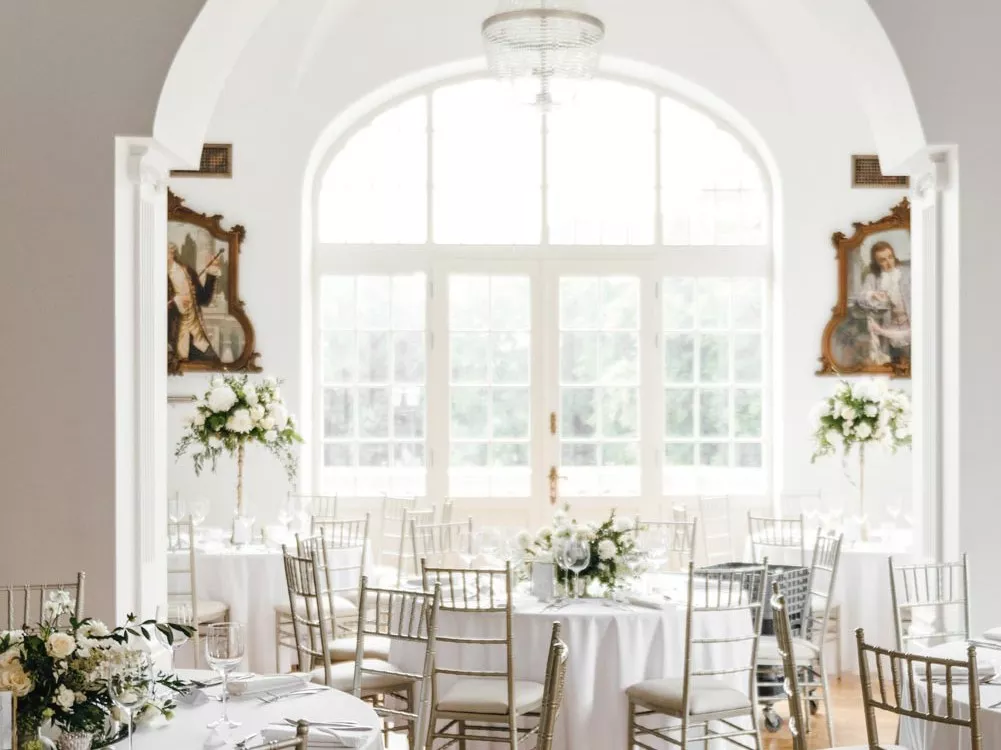 A pyramid stack of empty crystal champagne coupe glasses on a glass table with a dark background and soft lighting.