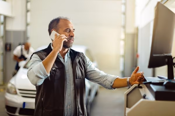 Homem falando ao celular enquanto mexe no computador para acessar o site administrativo Jump Car.