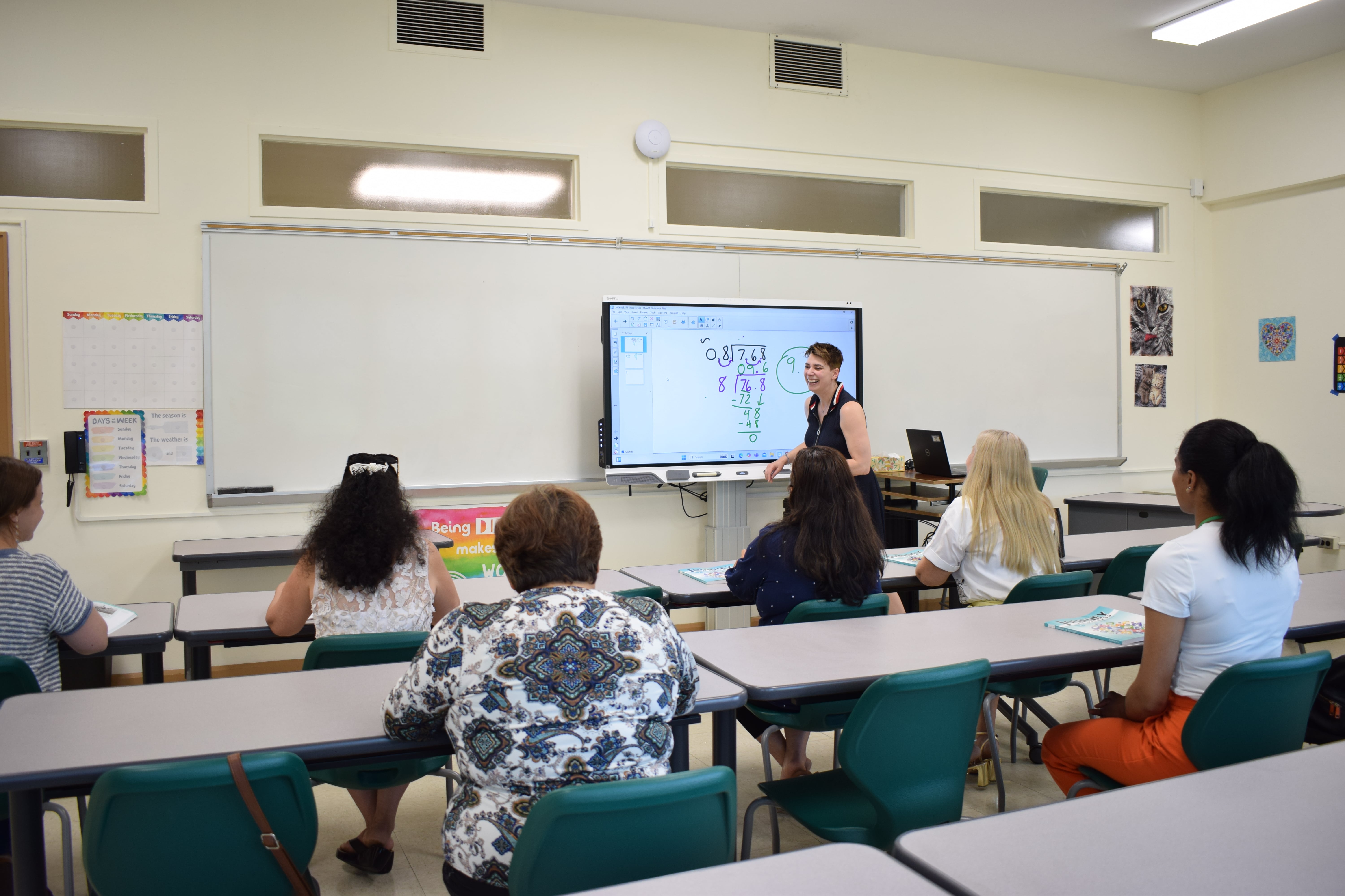 The teacher is reading from the board and asks students to repeat after her. 