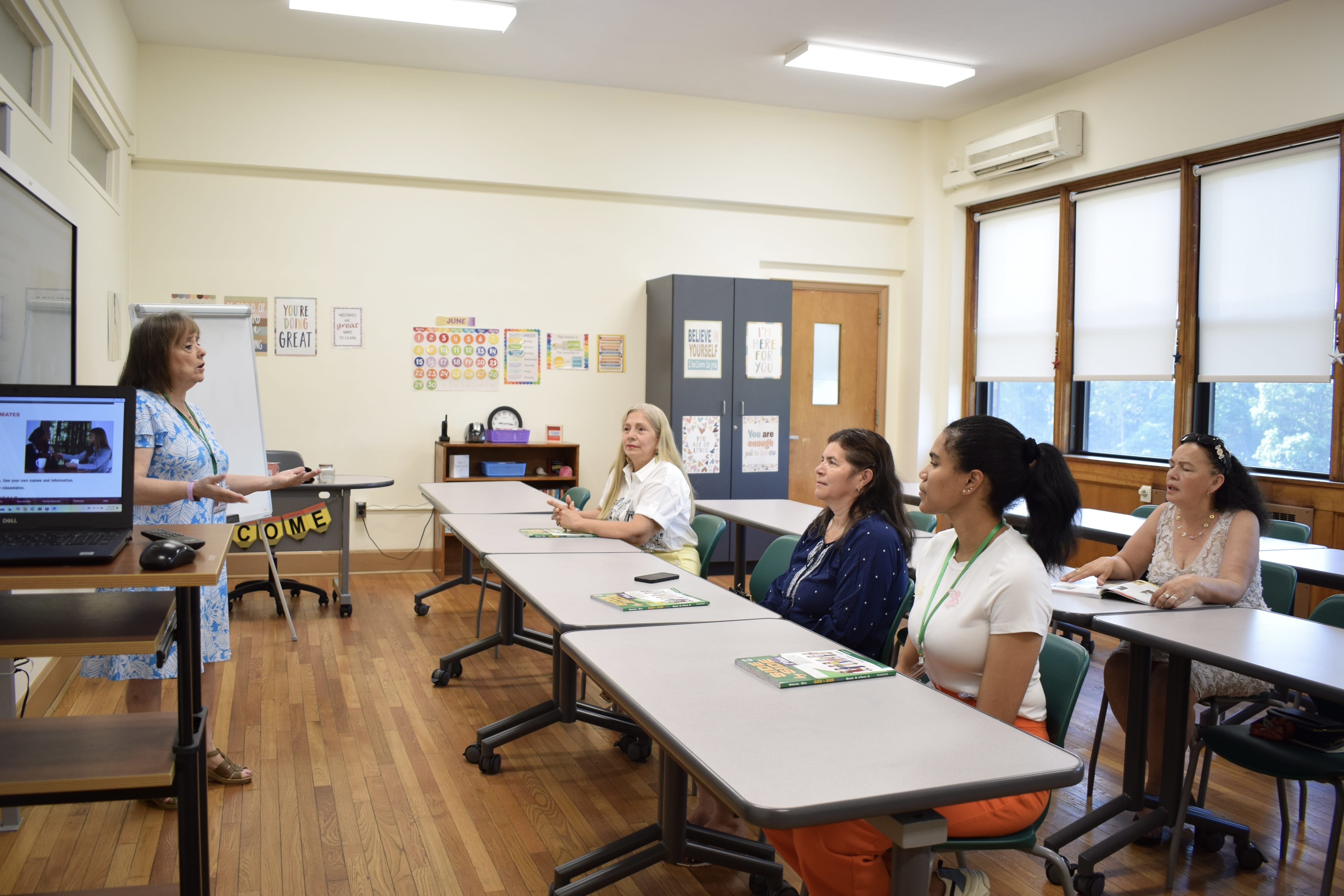 A full view of the classroom with students sitting at the desks and listening to the teacher. 