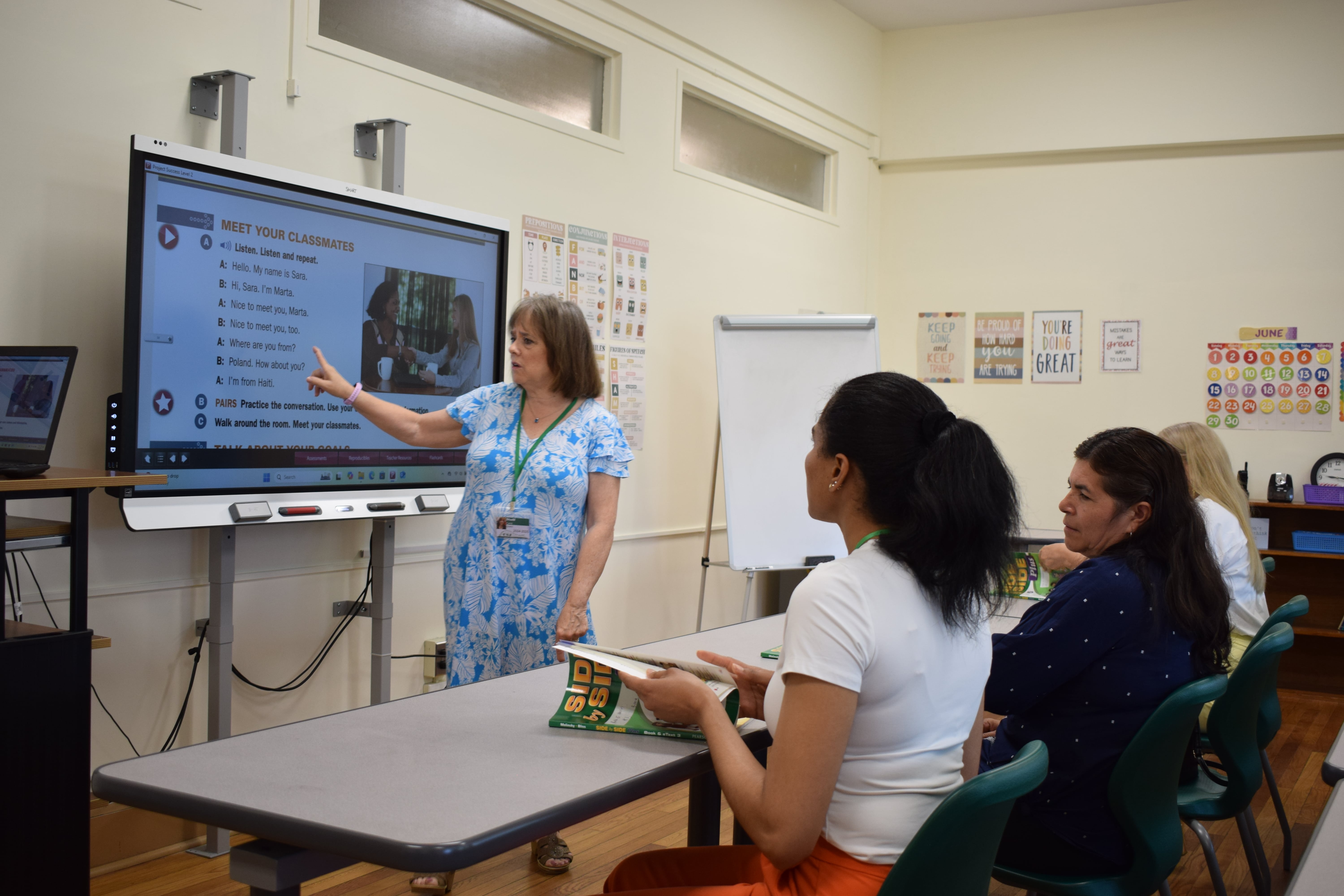 The teacher is pointing at the board and explaining the English sentences to the students. 