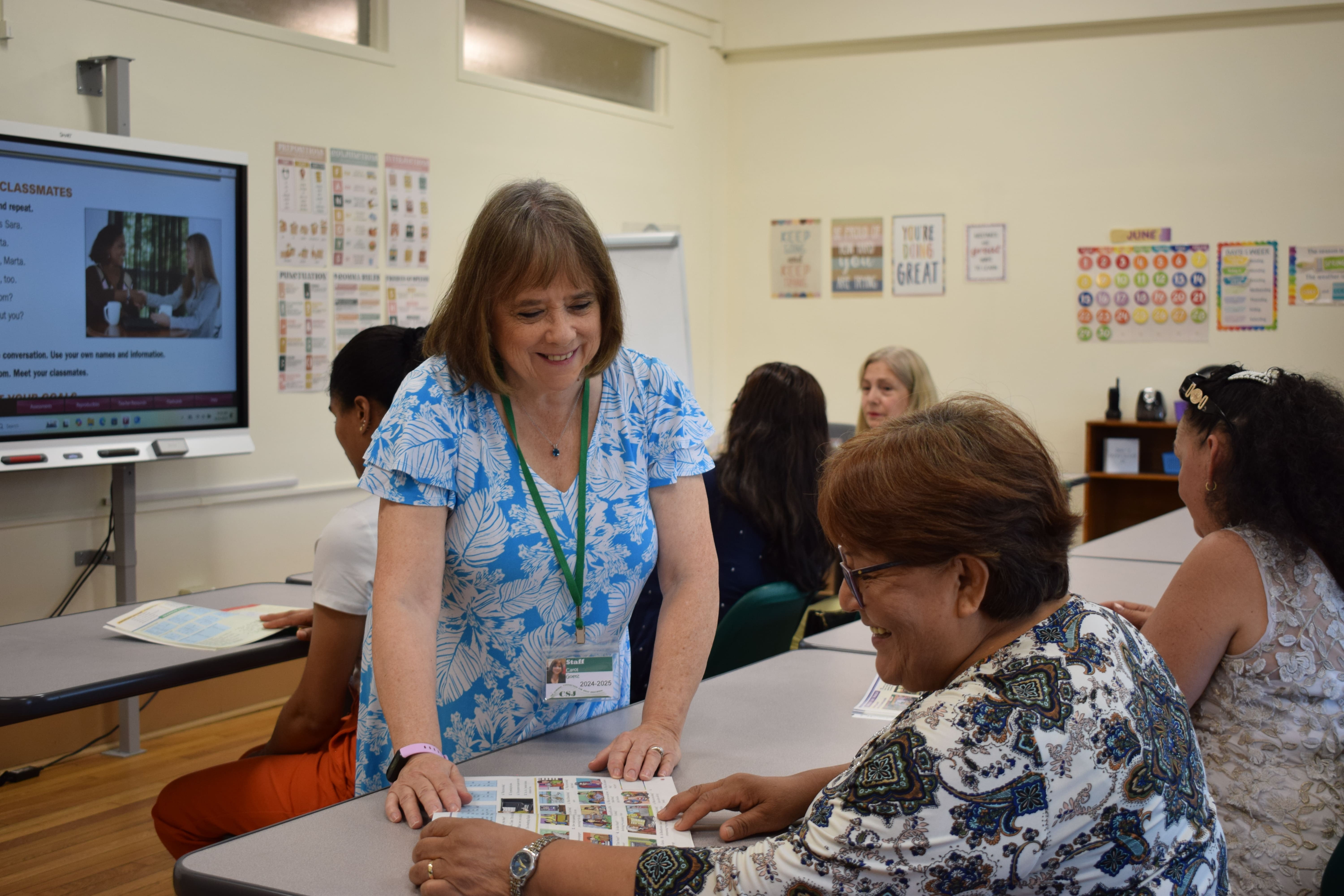 The teacher is explaining the material to two students, and they're smiling. 