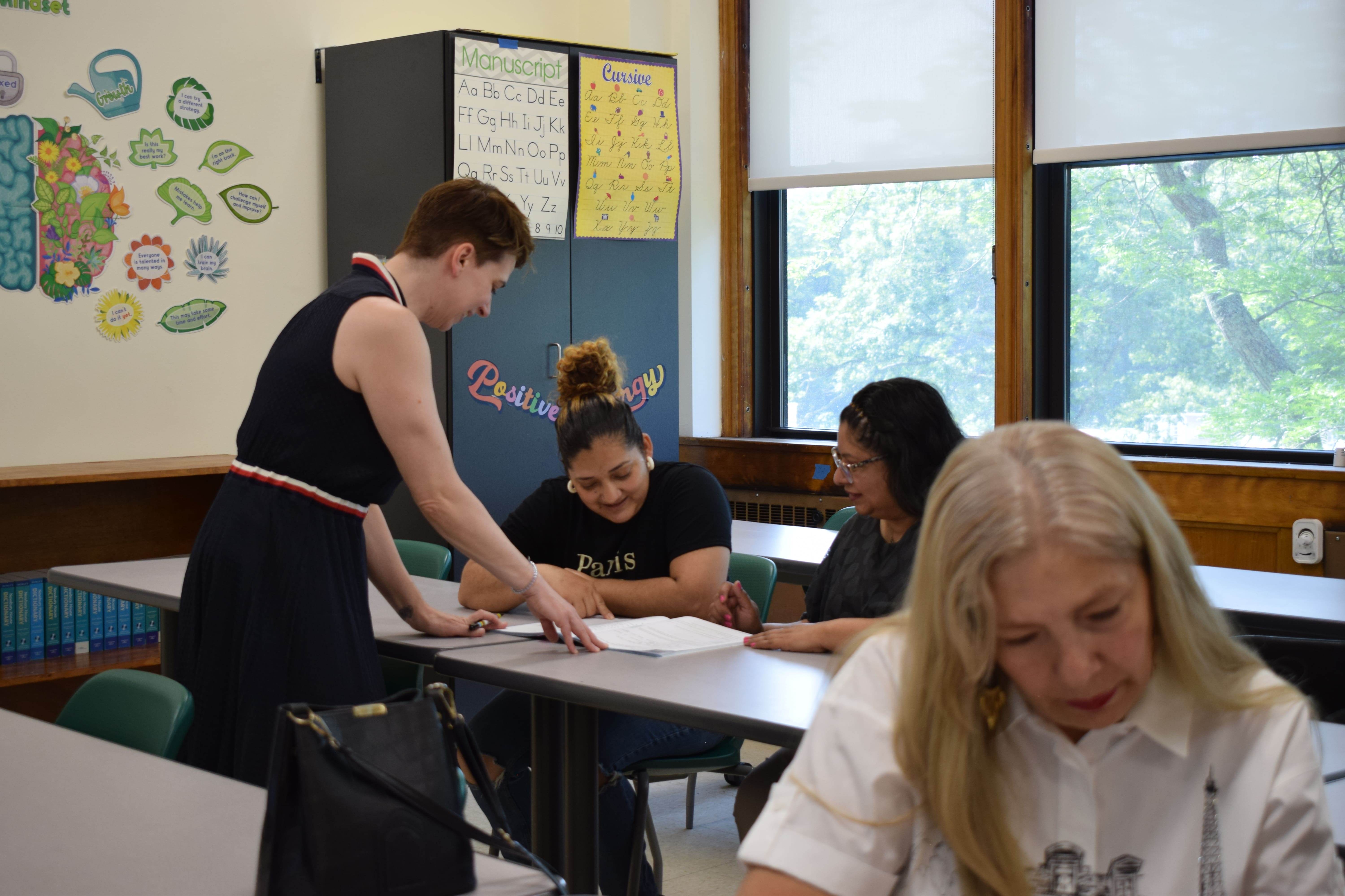 A teacher assisting students in a classroom while explaining a lesson.