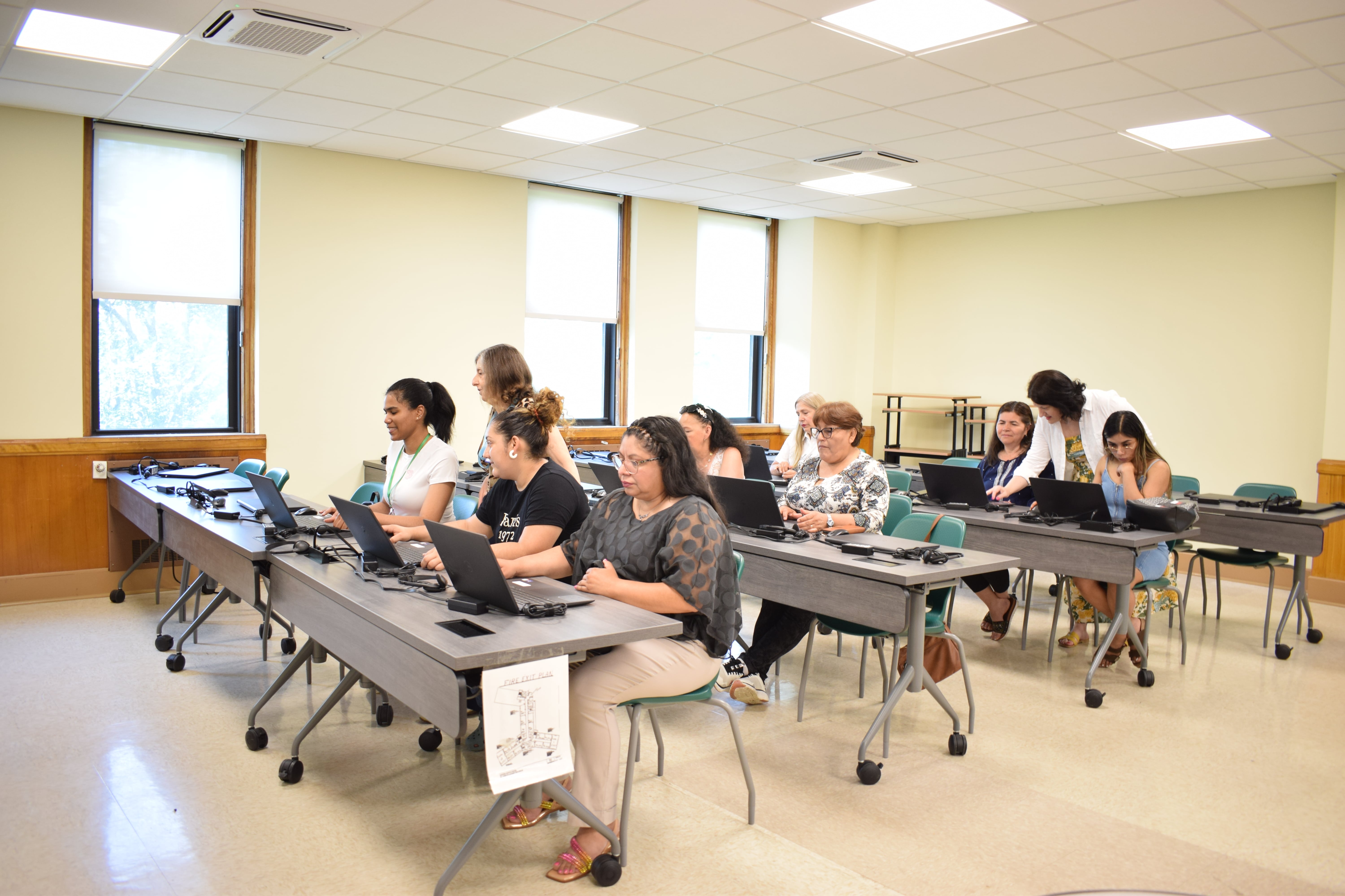 Students are sitting at desks in a large classroom, listening attentively to the teacher.
