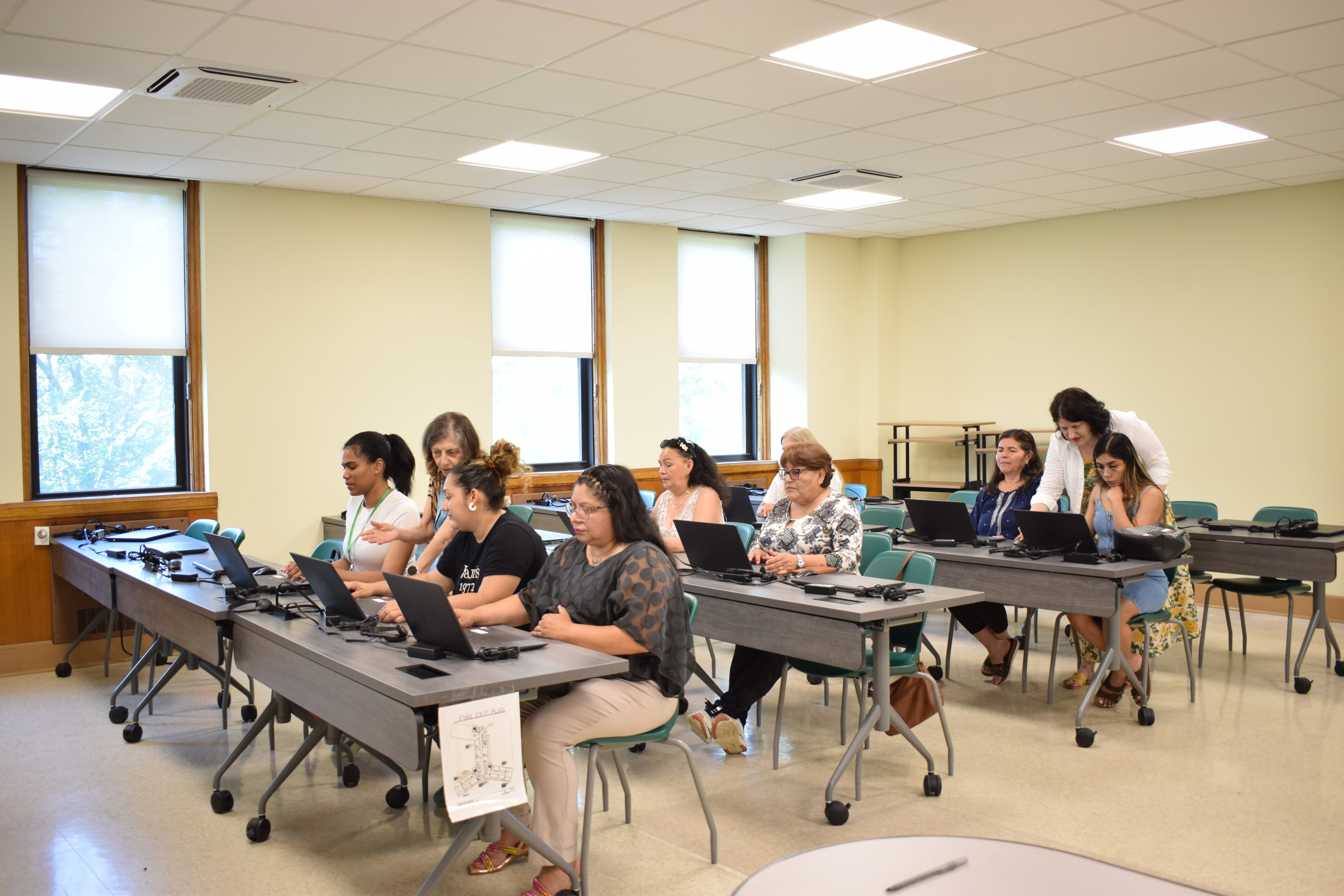 Students are sitting at desks in a large classroom, listening attentively to the teacher.