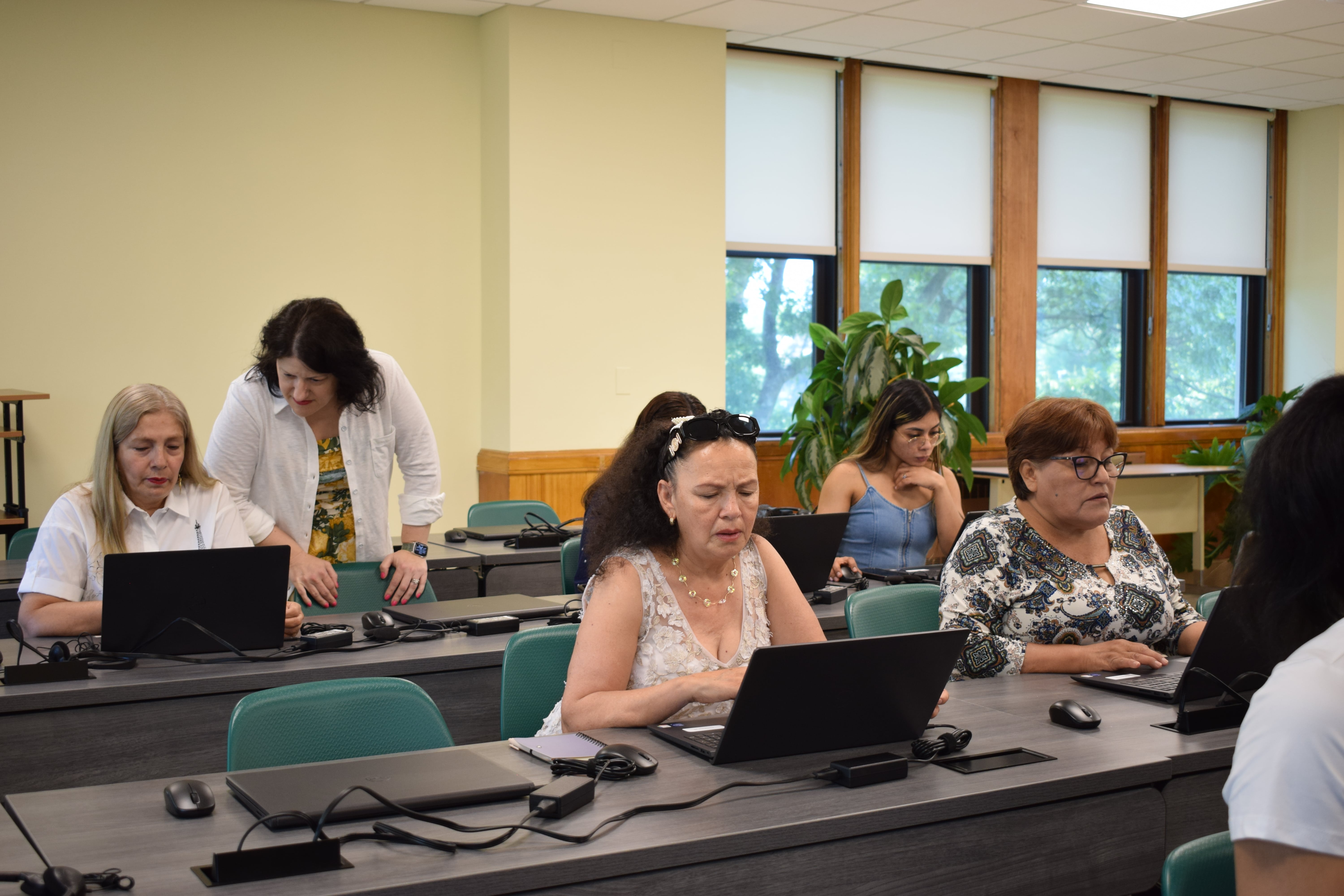 The teacher is assisting the students in a computer classroom, guiding them on their assignments.