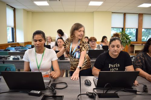 Teacher assisting two students in a computer classroom, guiding them on their assignments.