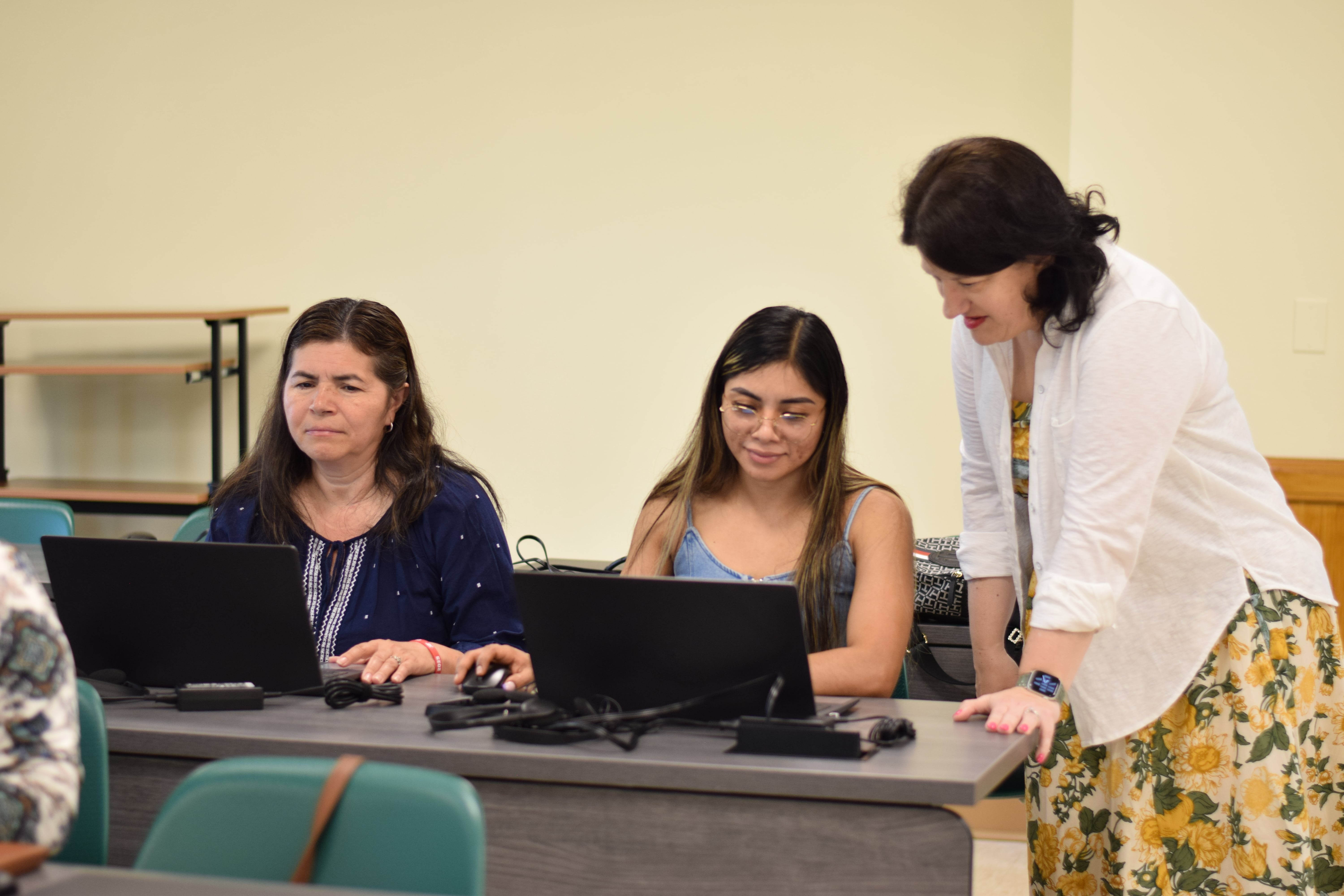 The teacher is assisting a student with a computer assignment, looking at the screen together.