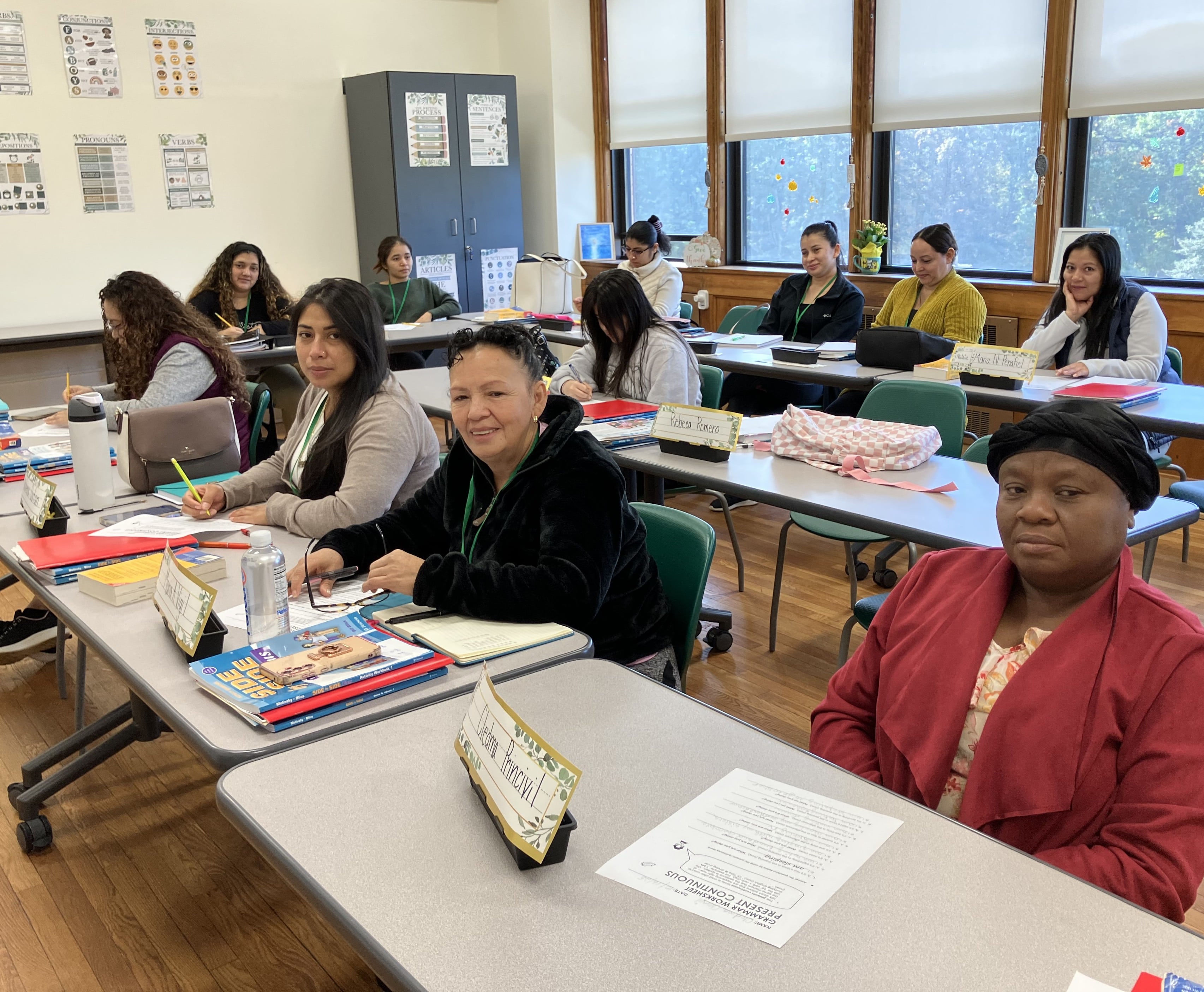 Women studying in a classroom, reading from the paper, and listening to the teacher during English as a New Language class. 