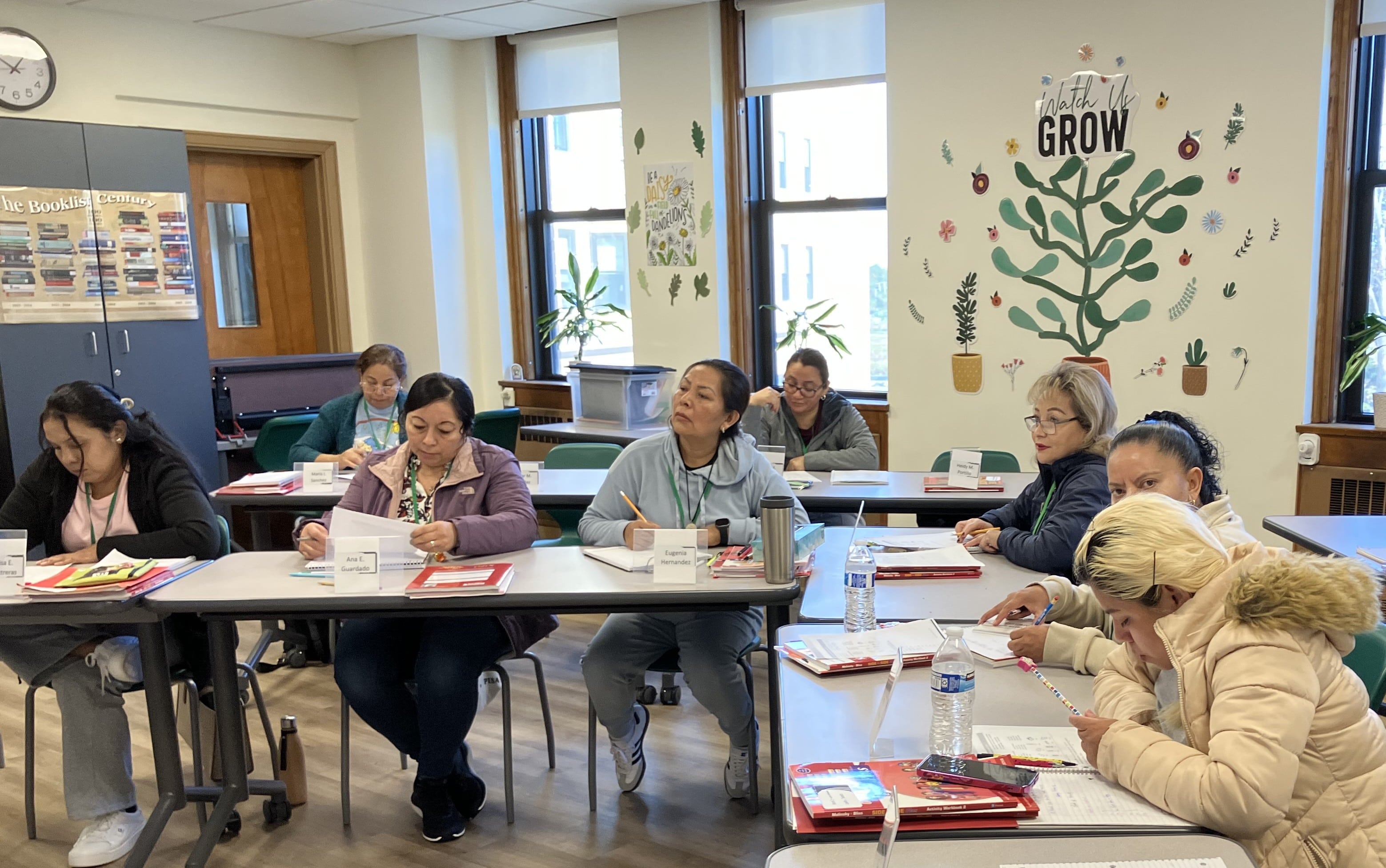 Students sitting at desks, reading and listening attentively, with the TLC tree displayed on the wall behind them.