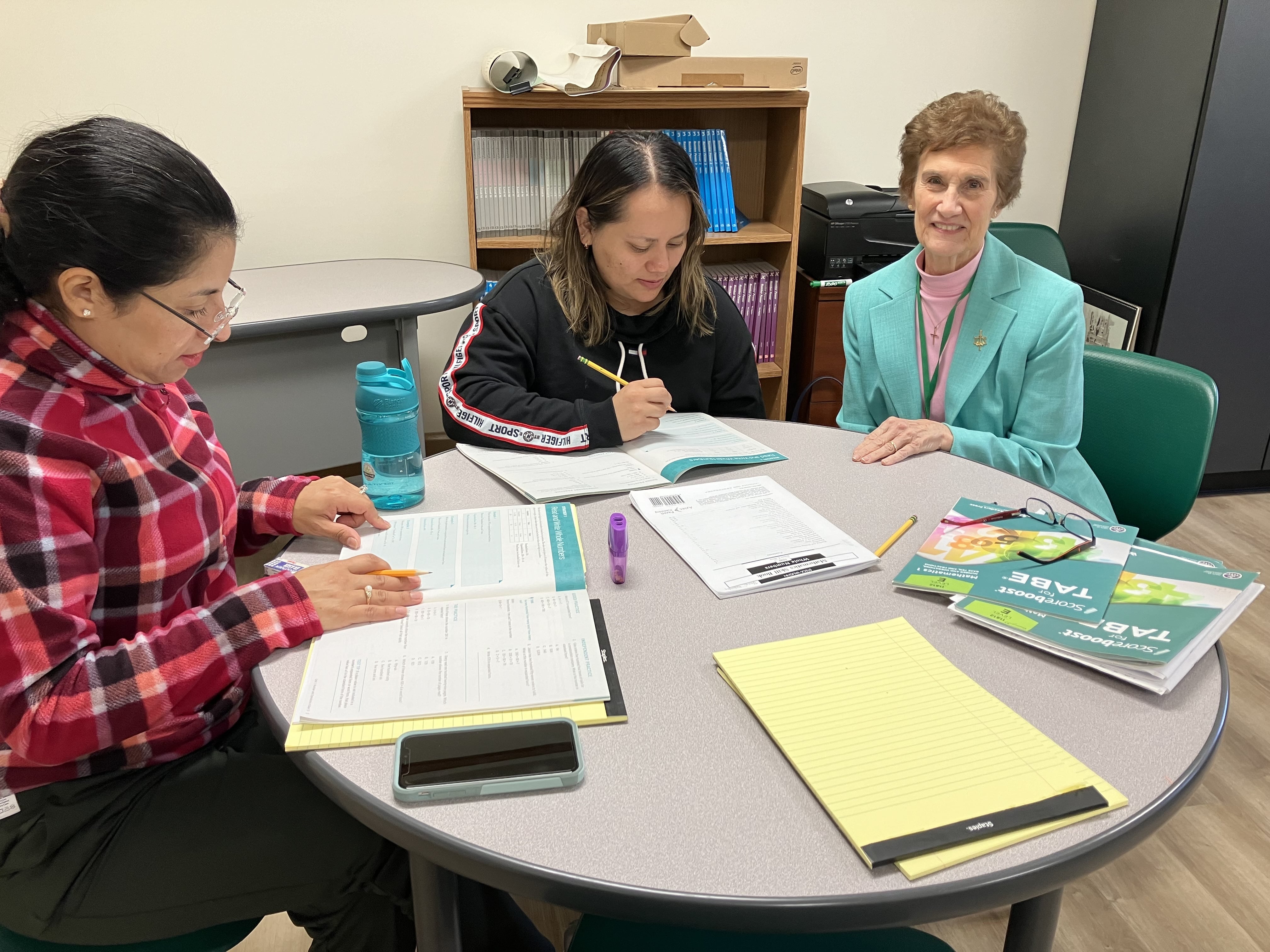 Sister Jean Amore is teaching two students sitting at the table. 