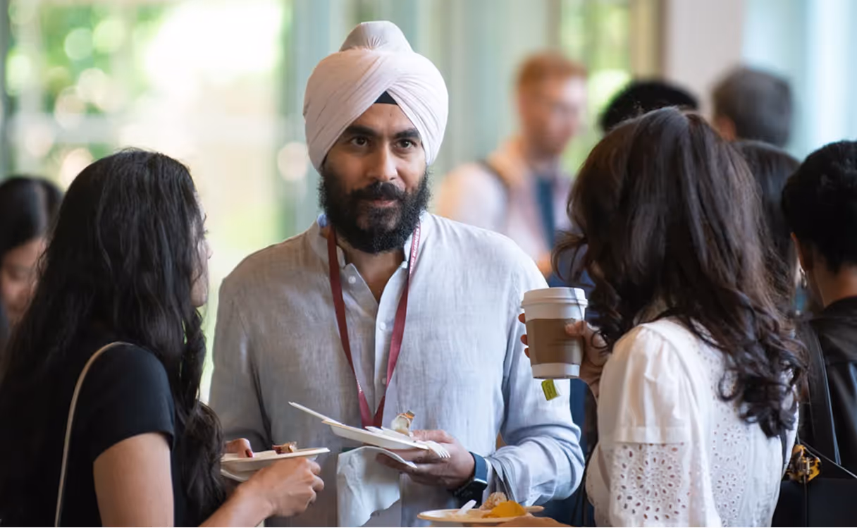 A man wearing a turban and a red lanyard is holding a plate of food.