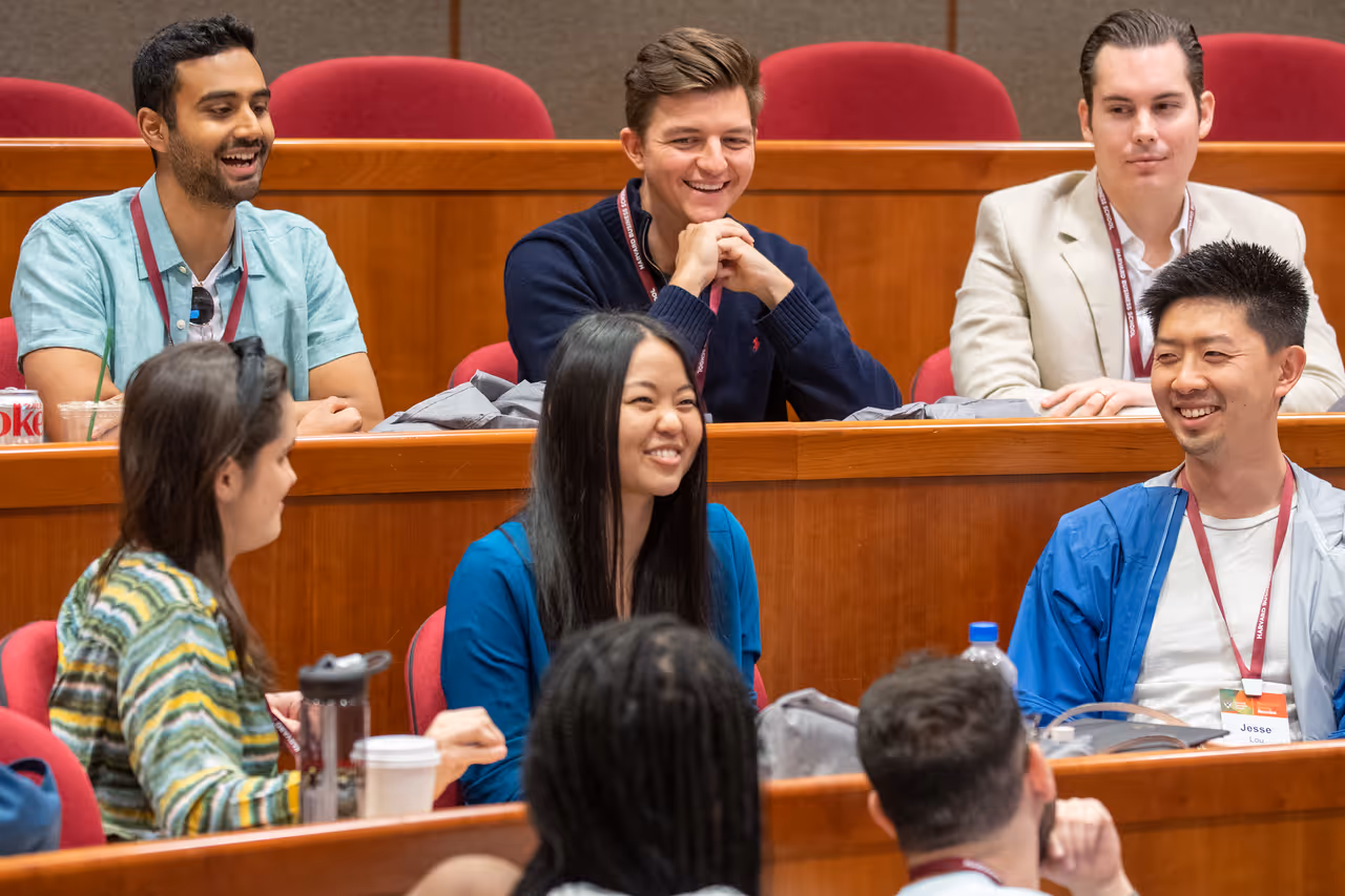 tudents laughing and engaged in a discussion in an MBA lecture hall with tiered red seating.