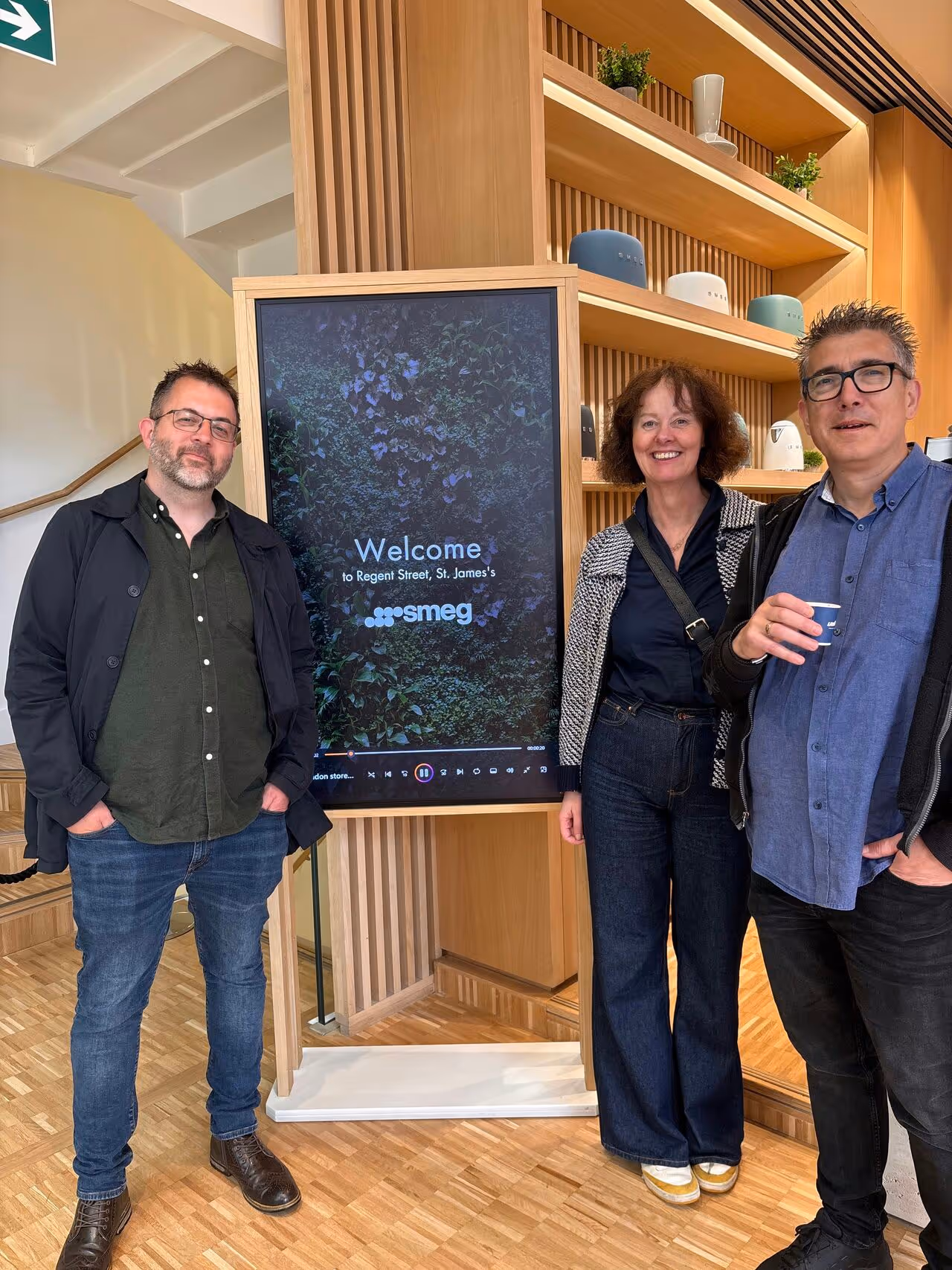 Three people standing near Smeg welcome screen in modern wooden interior