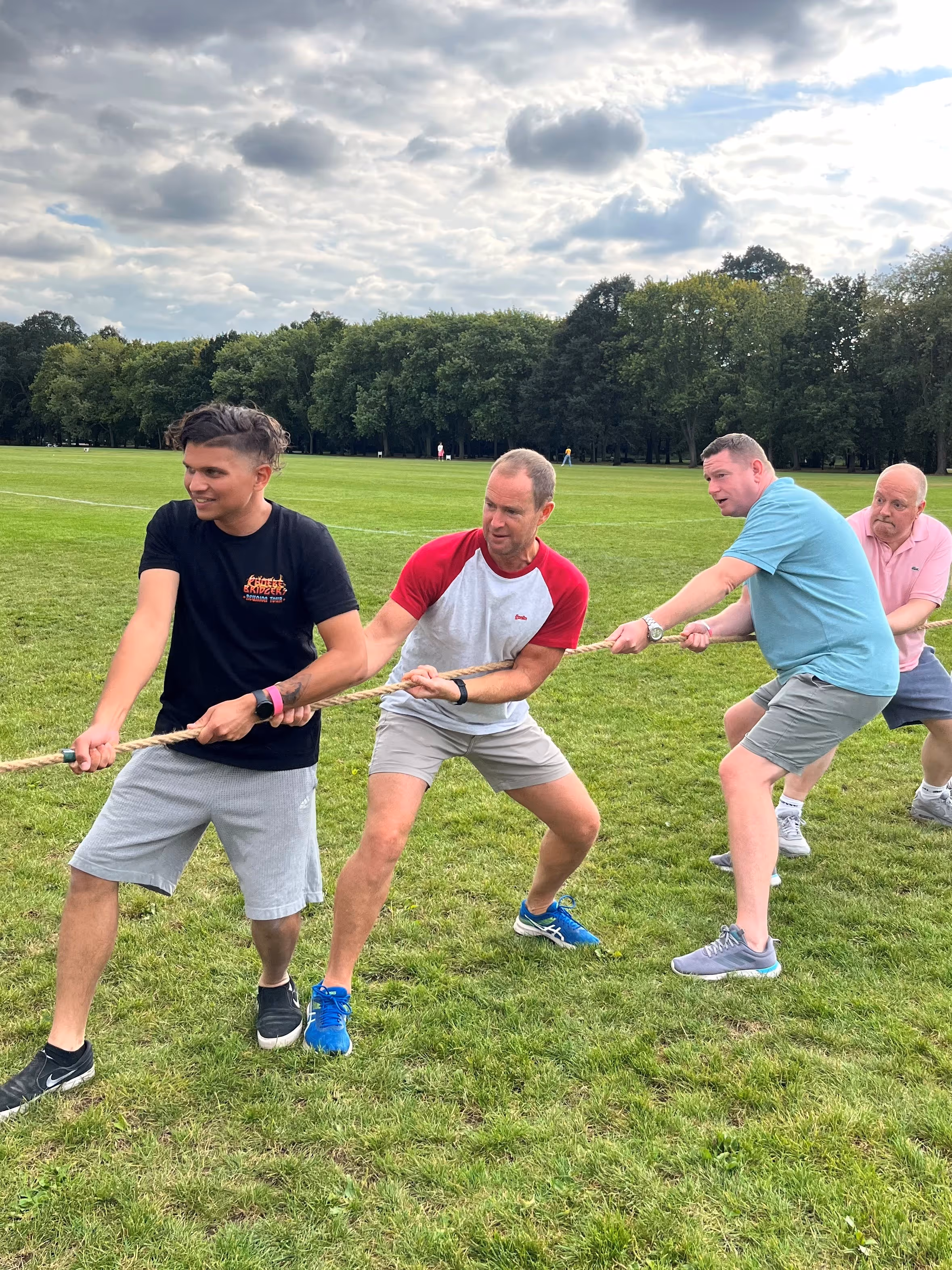 Men playing tug of war on a grassy field on a cloudy day