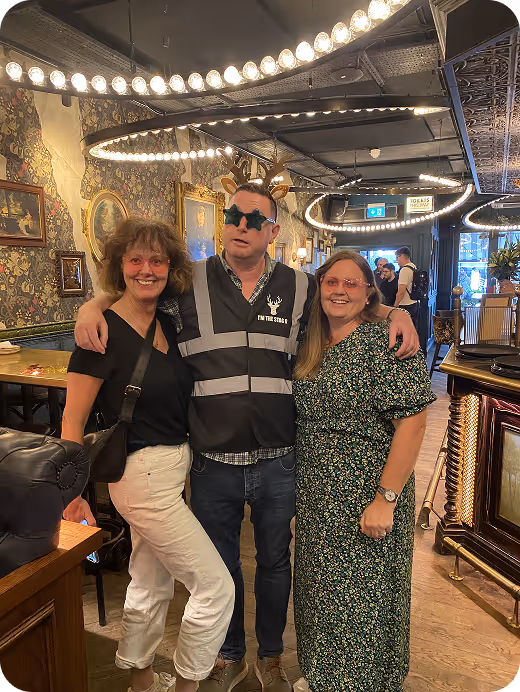 Three people posing together in a vintage-styled bar with string lights