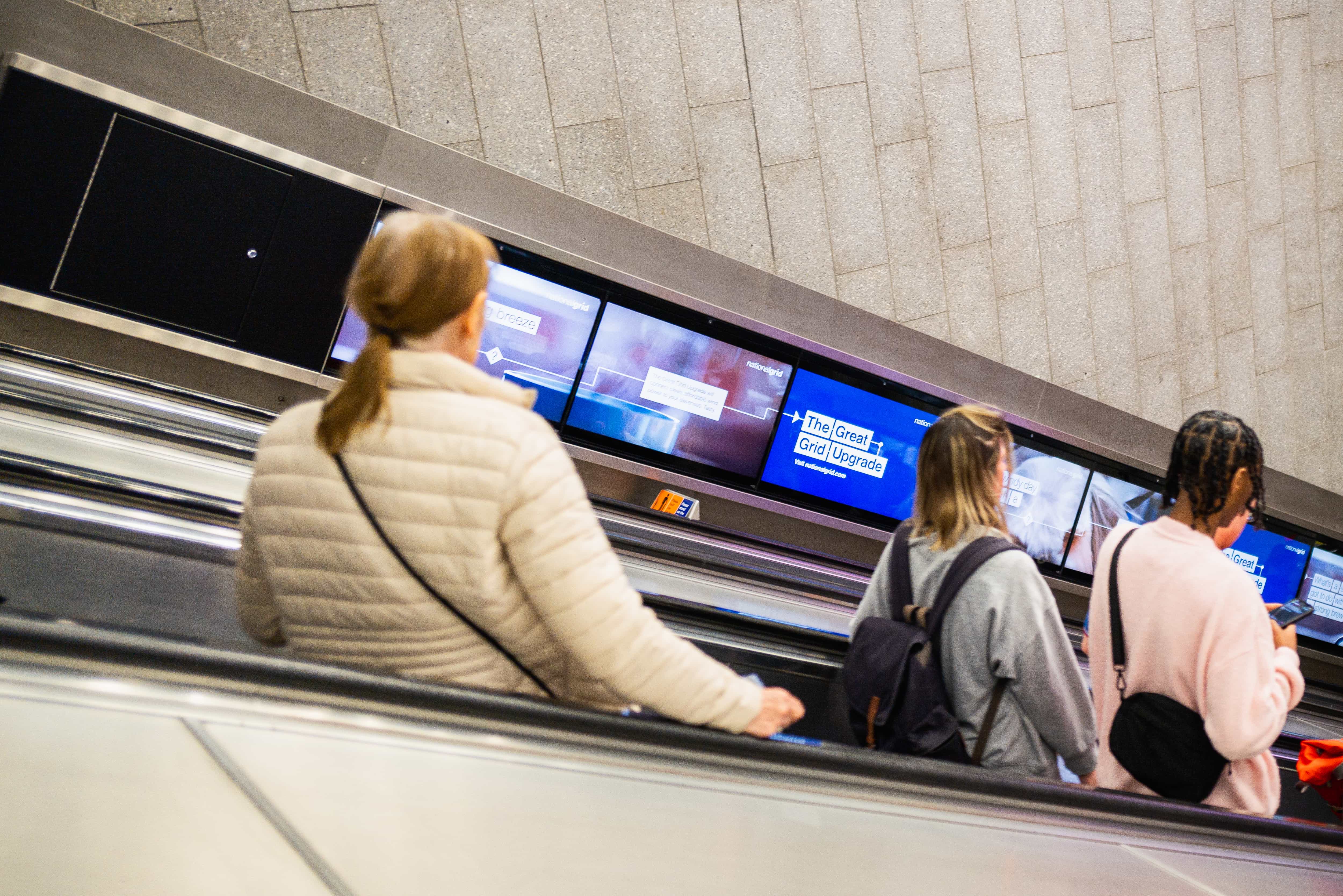 People riding escalator with digital screens showing "The Great Upgrade"
