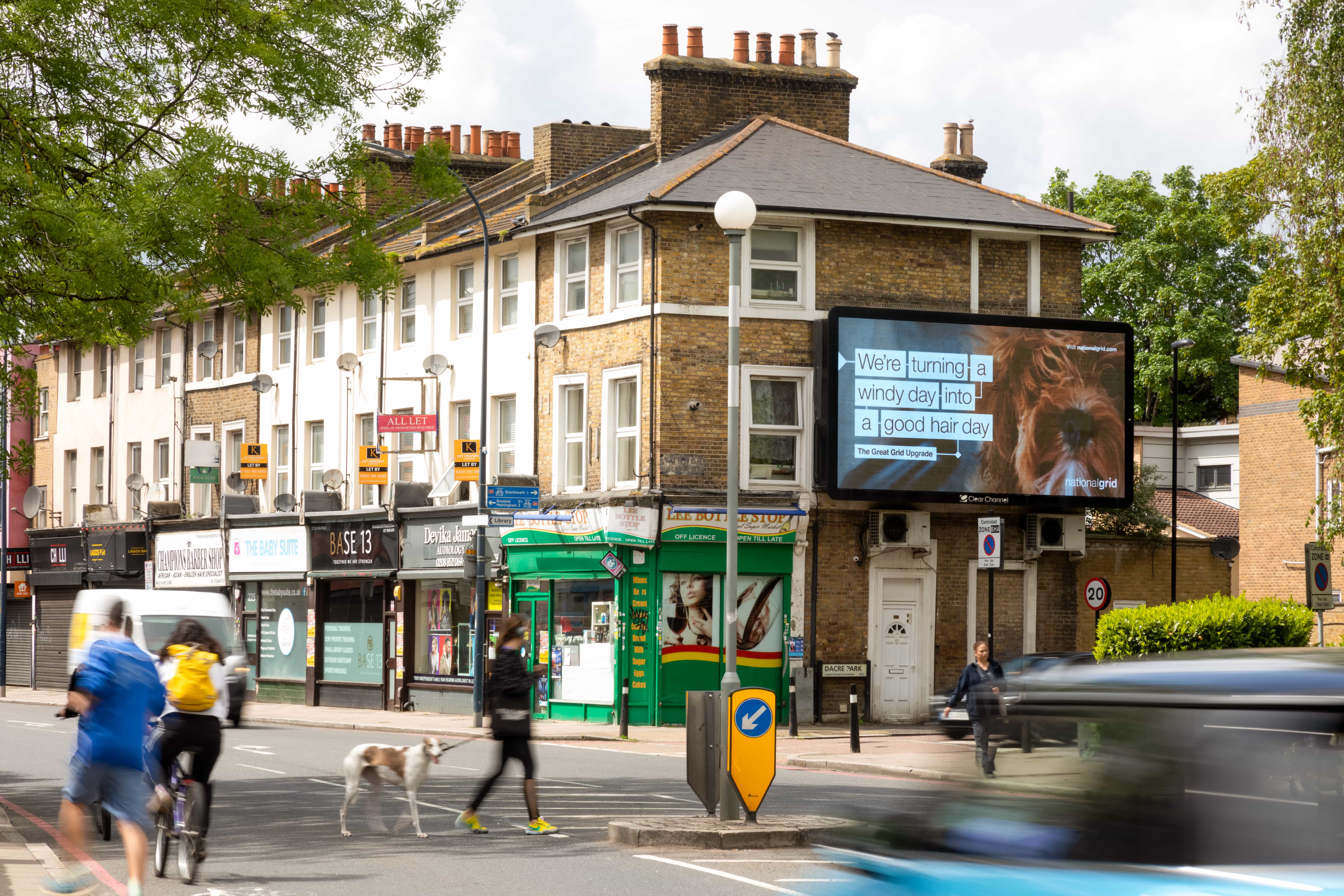 Busy urban street with cyclists, dog, digital billboard, and brick buildings