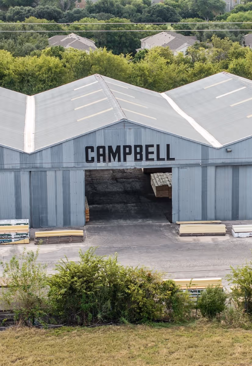 Large blue-gray Campbell warehouse with open doorway and stacked lumber materials