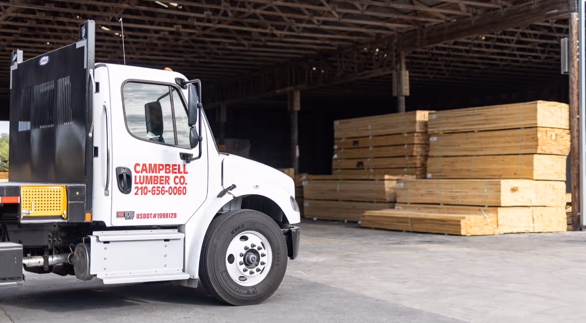 White Campbell Lumber Co. truck parked next to stacked lumber inside warehouse