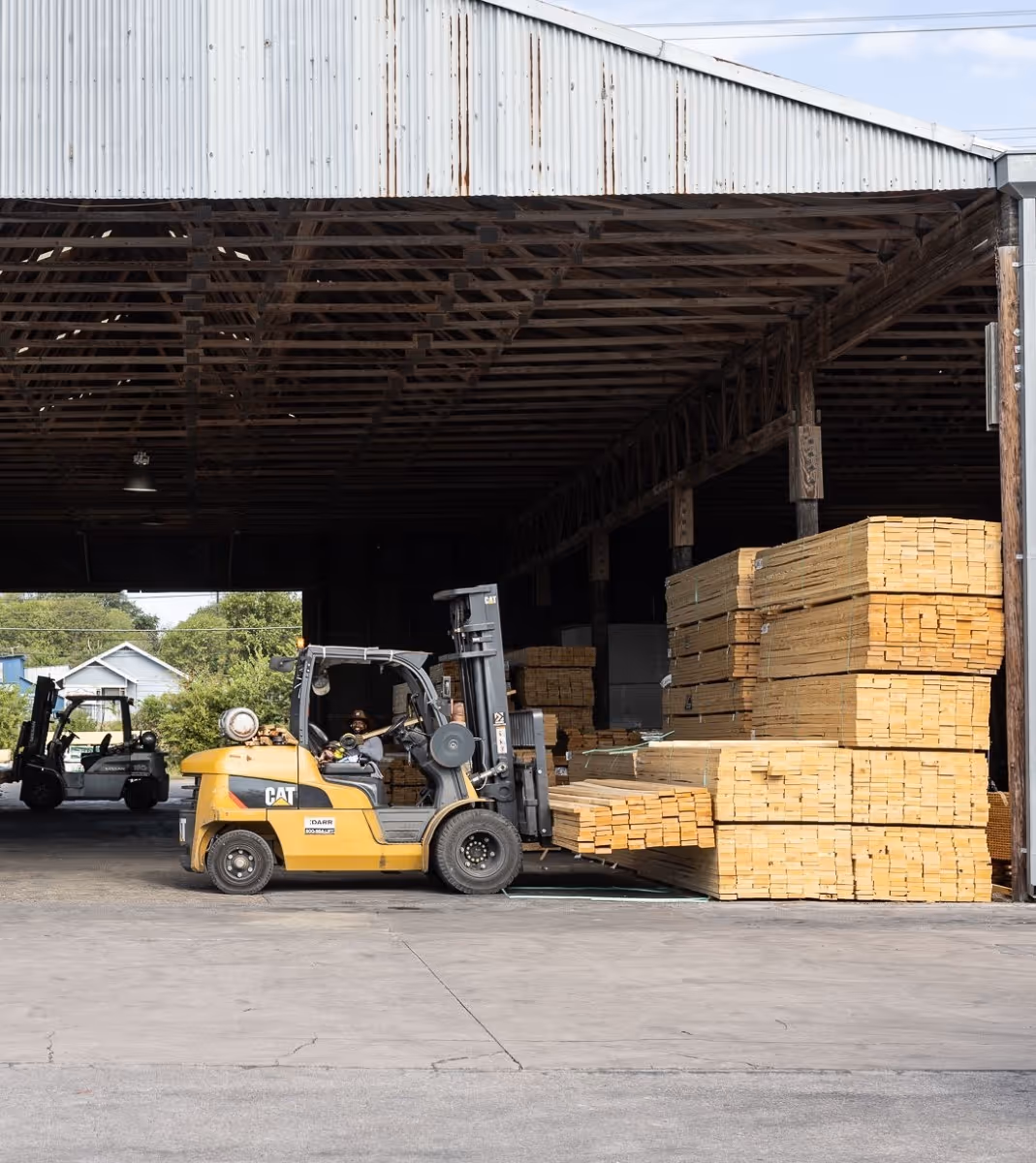 Yellow forklifts moving stacks of lumber in a warehouse storage area