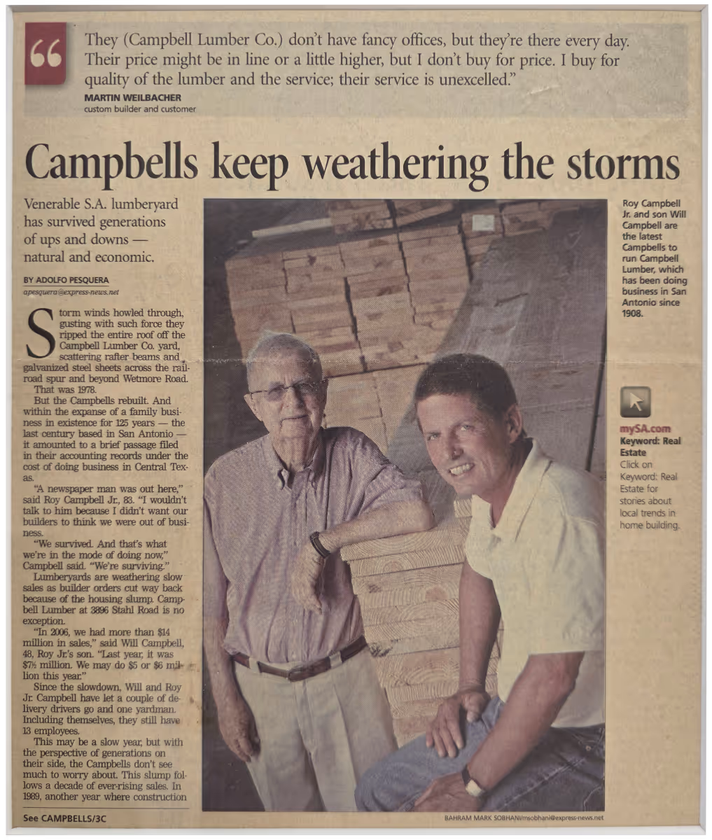 Two generations of Campbell Lumber Co. standing with stacked lumber