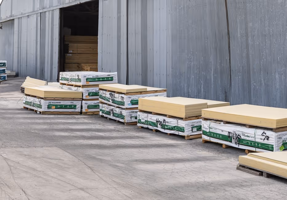 Stacked wooden boards and pallets outside a metal warehouse building