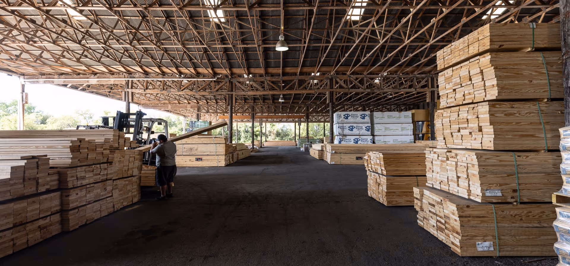 Lumber warehouse with stacked wooden boards and forklift