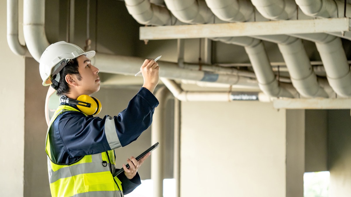 Inspector with a tablet checking overhead pipework