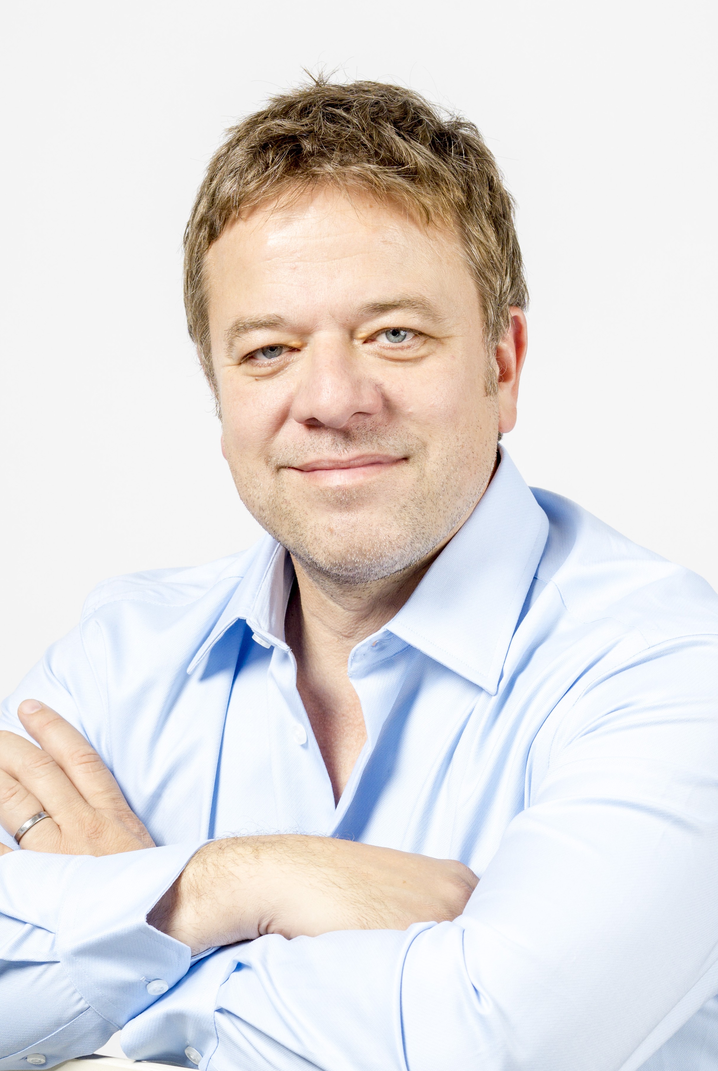 A headshot of Jonathan, a white journalist, with a blue shirt. He has his arms crossed and there is a white background