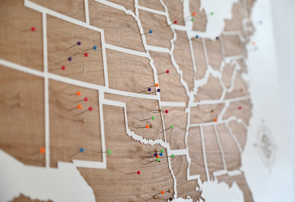 Wooden map of the United States with multicolored pins marking various locations.