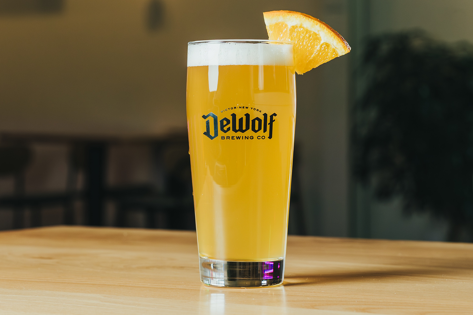 A hazy golden pour of The King's Wit Witbier garnished with a fresh orange slice in a DeWolf Brewing Co. glass, Victor New York