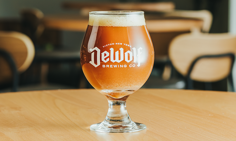 A glass of Foggy Goggles winter warmer from DeWolf Brewing Company, amber with a creamy white head, served on a wooden table.