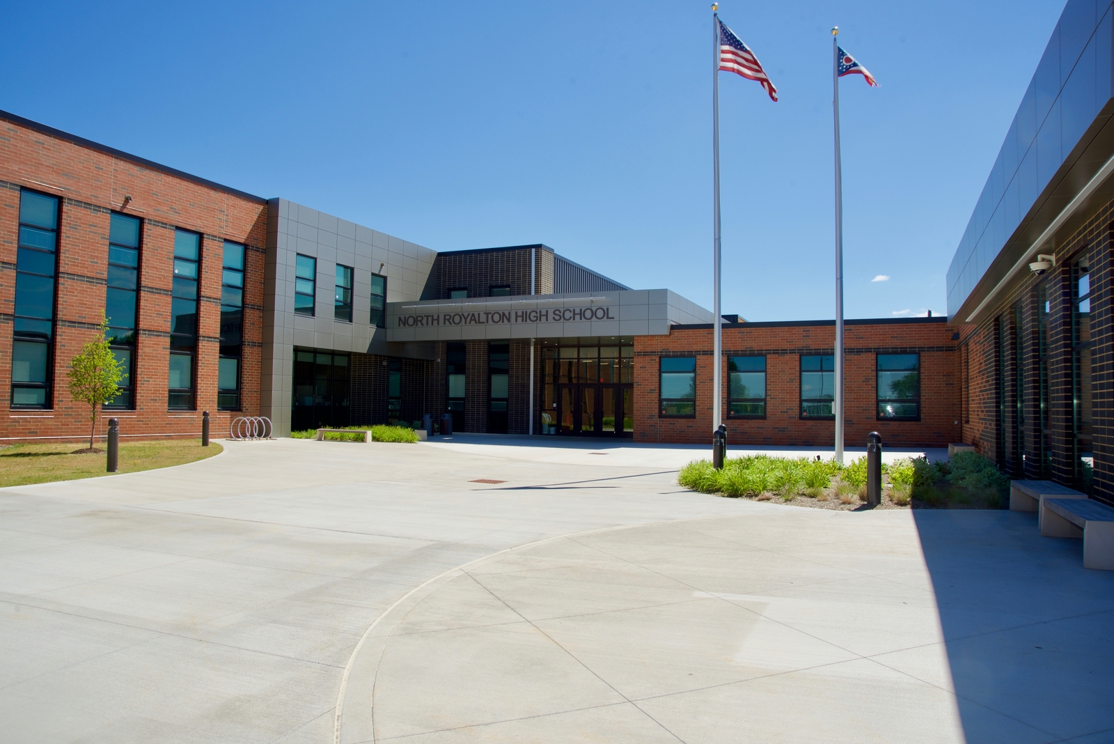 Front view of North Royalton High School building with American and Ohio state flags on flagpoles under a clear blue sky.