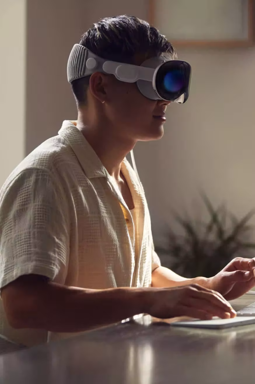 ผู้ชายใส่แว่นตาเสมือนจริงสีเทานั่งที่โต๊ะใช้แป้นพิมพ์