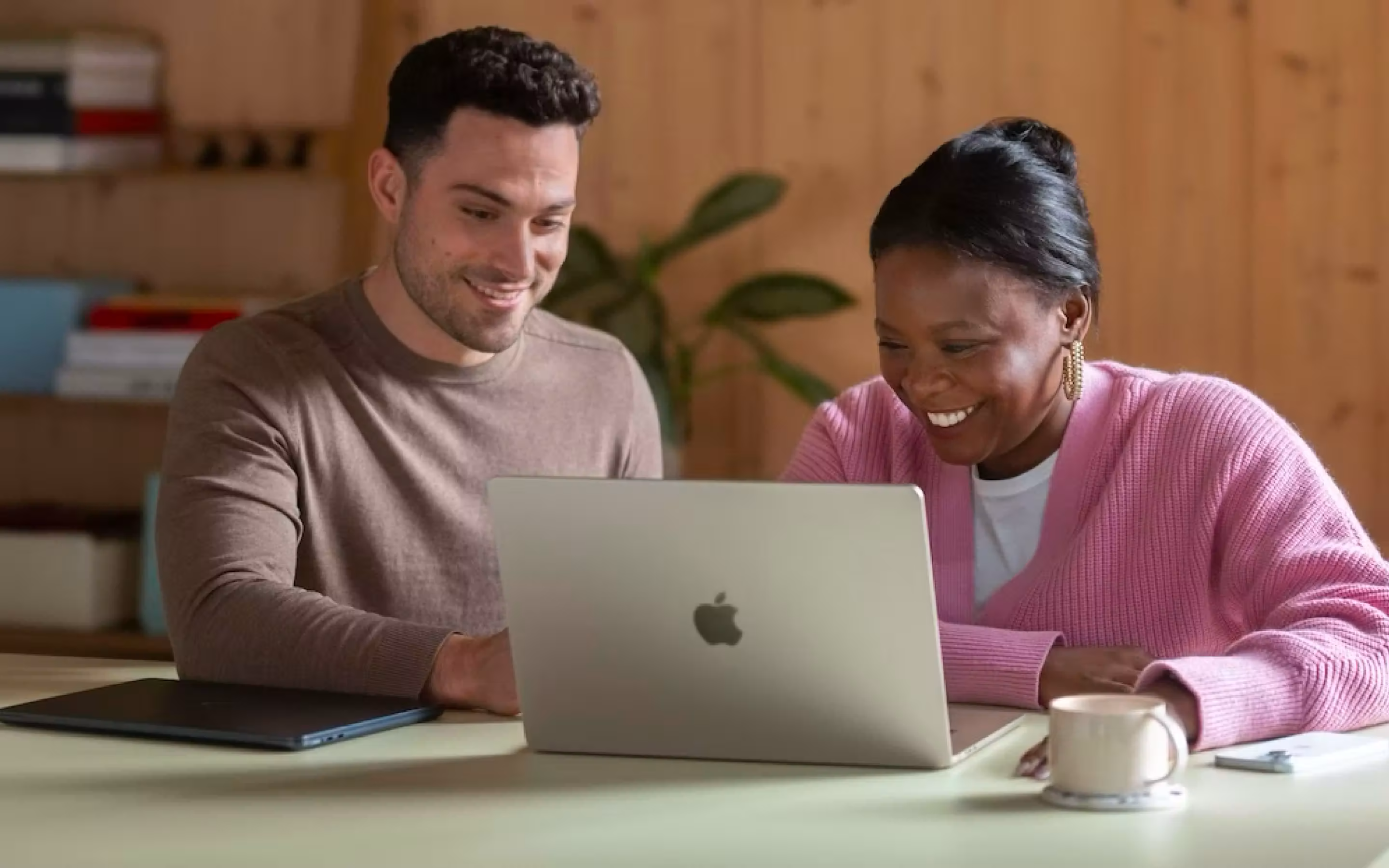 ผู้ชายและผู้หญิงนั่งร่วมกันที่โต๊ะกำลังดูแล็ปท็อปด้วยความสุข