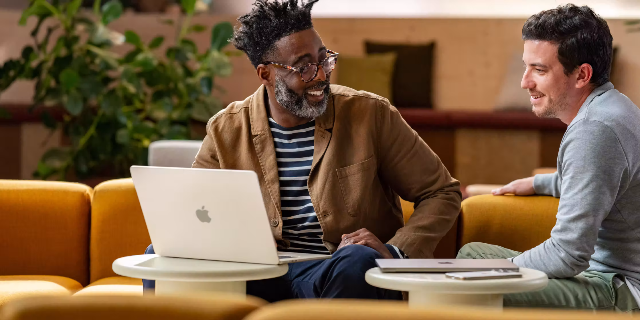 ชายสองคนกำลังนั่งพูดคุยอย่างเป็นมิตรในห้องนั่งเล่นโดยมีแล็ปท็อปวางอยู่บนโต๊ะด้านหน้า