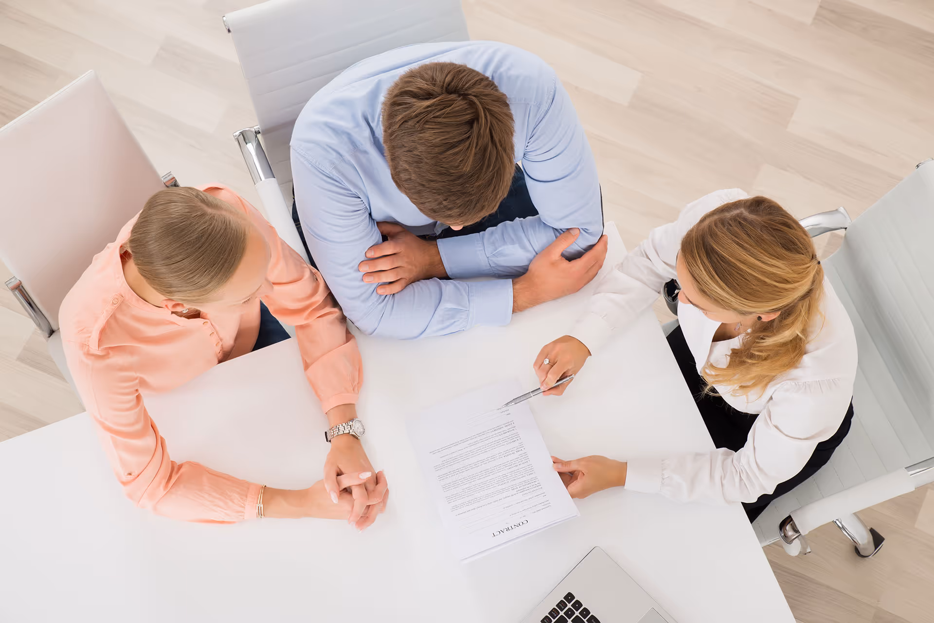 Three people sitting at a white table reviewing a contract document, one person pointing at it with a pen.