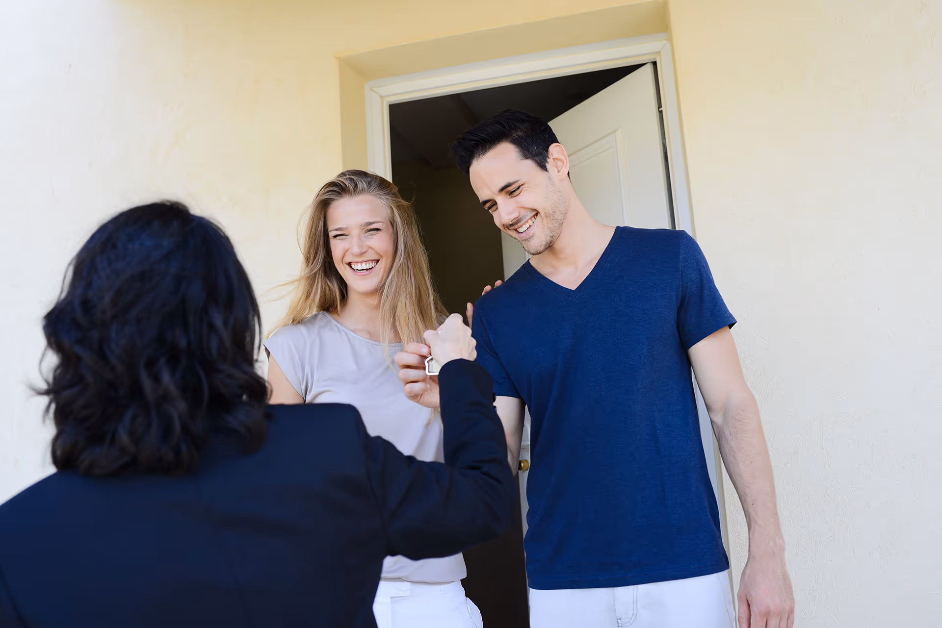 Smiling couple receiving house keys from a real estate agent at the doorway.