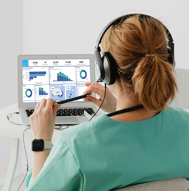 Healthcare professional in green scrubs and headset reviewing patient data and charts on a laptop screen.