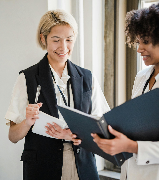 Two professional women smiling and reviewing documents together indoors.