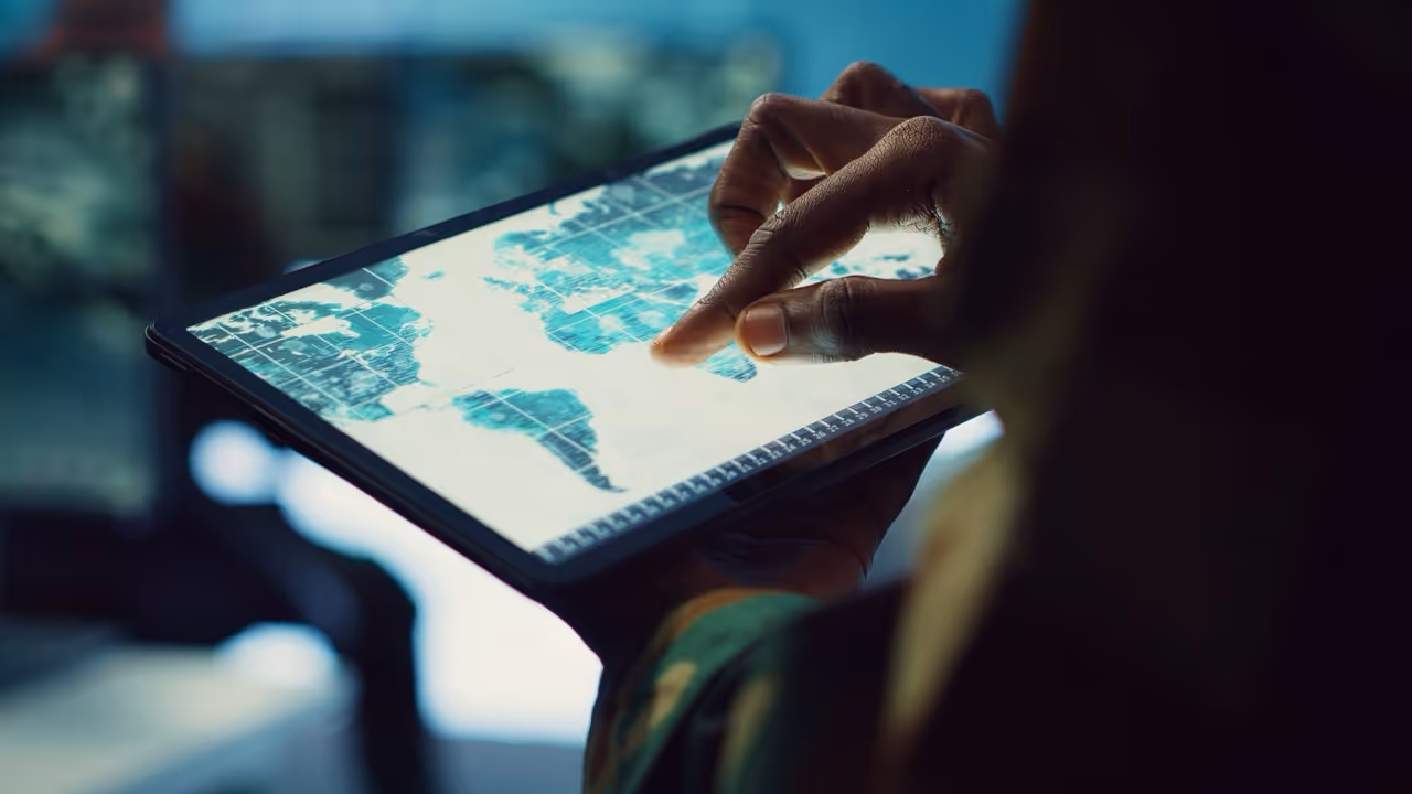 Person's hand interacting with a world map displayed on a tablet screen.