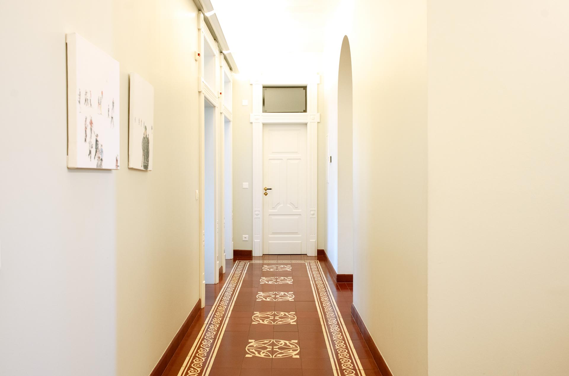 Corridoio luminoso con pavimento in piastrelle rosse decorate e porta bianca alla fine.