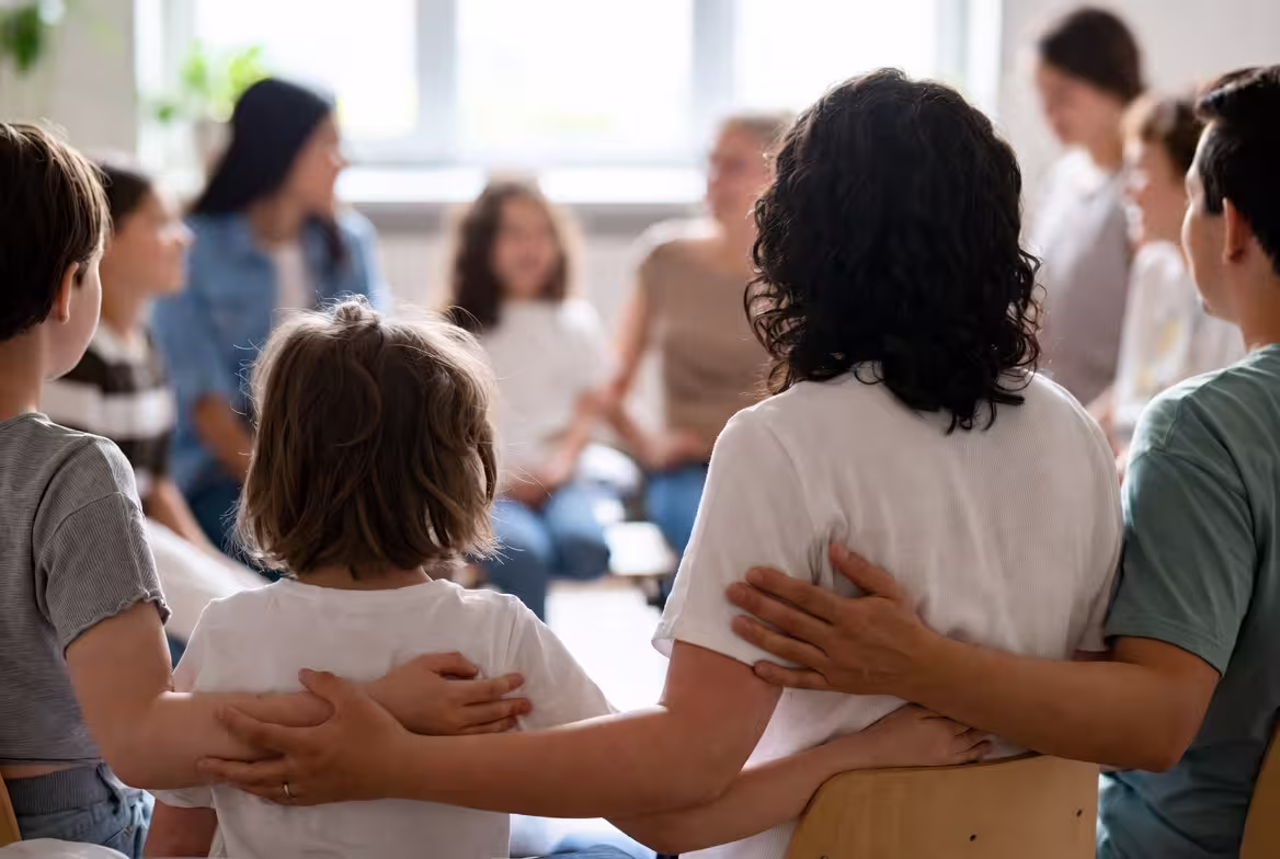 Families gathered in a support group setting with a child seated near the center.