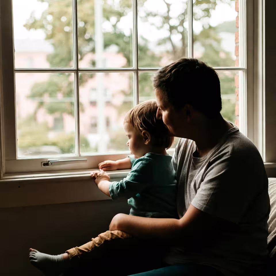Parent sitting with a child by a window during a quiet caregiving moment.